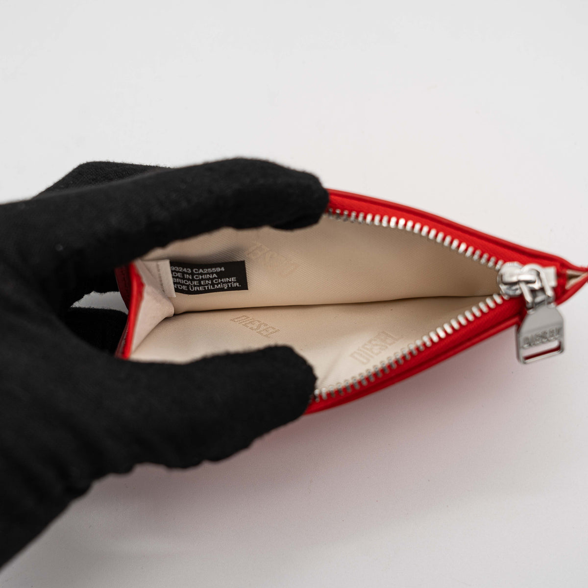 Diesel red patent card holder with silver logo plaque and top zip, set against a clean background.