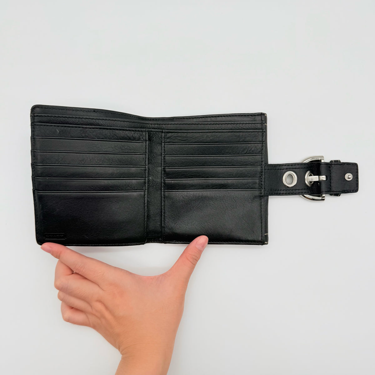 Coach black Soho Bifold Wallet with signature silver buckle and contrast stitching, shown closed against a white background.