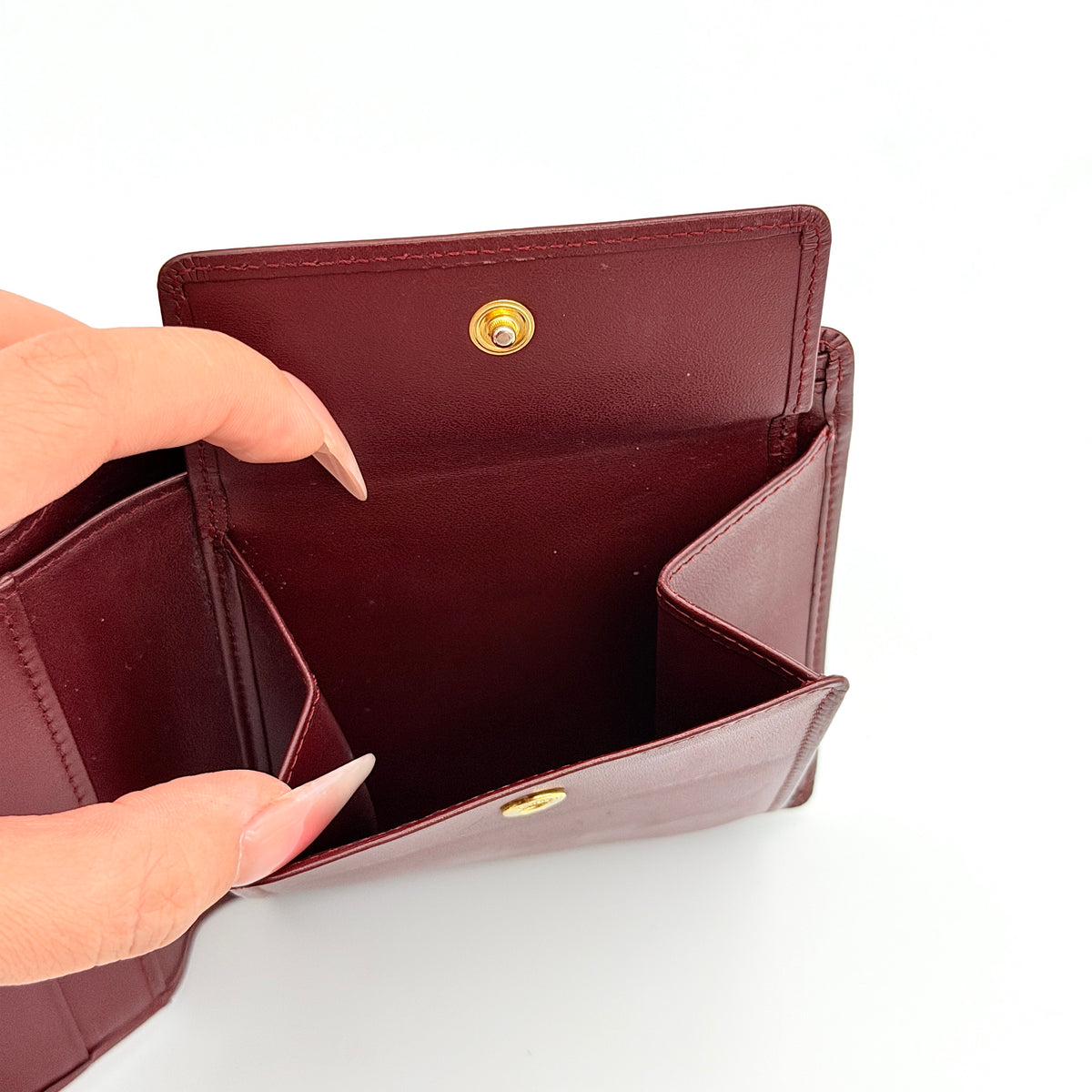 Cartier Must de Cartier bifold wallet in burgundy leather with gold-tone corners and embossed logo, photographed against a white background.