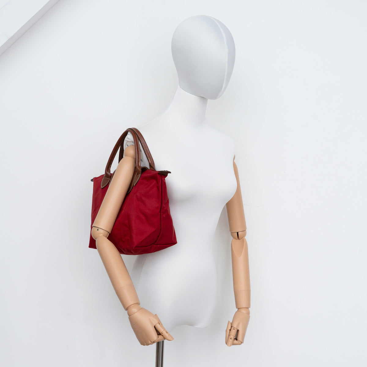 Longchamp Le Pliage handbag in red nylon with brown leather handles and gold-tone accents, photographed on a white background.