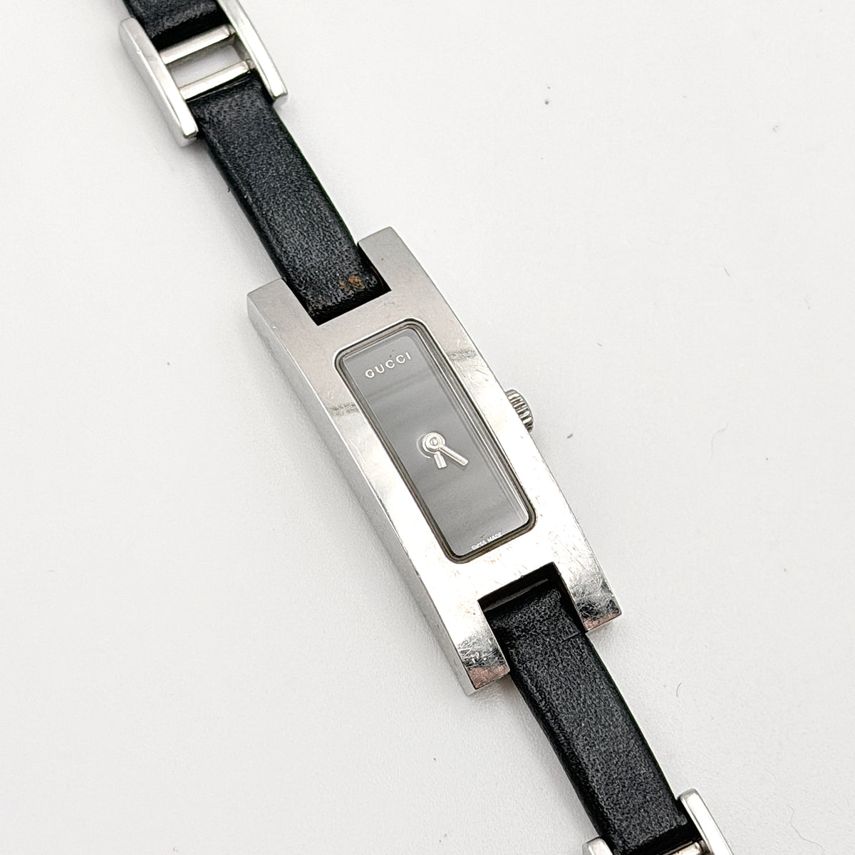 Gucci 3900L black dial watch with silver-tone rectangular case and black leather strap displayed on a stand