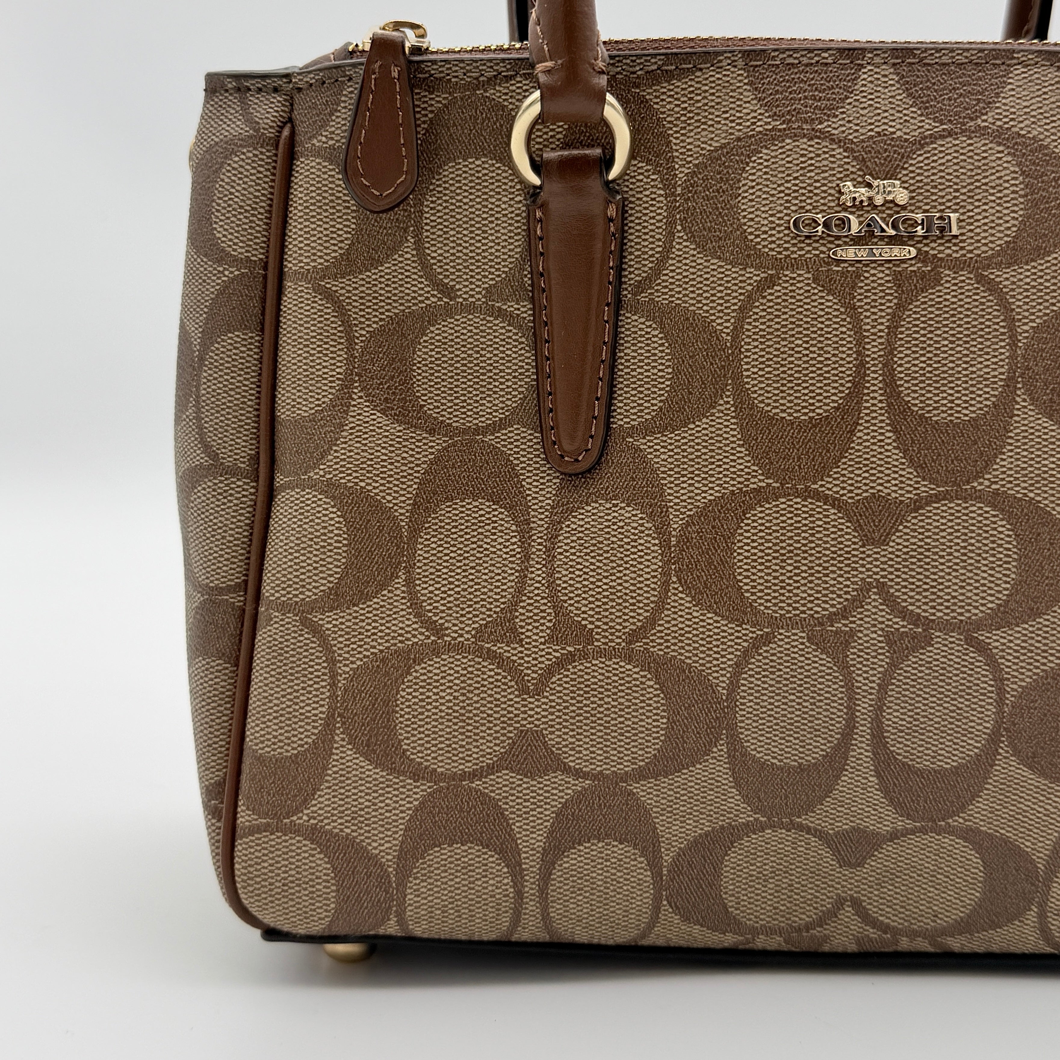 Coach Christie Carryall in beige and brown canvas with gold hardware and detachable strap, photographed in a studio setting.