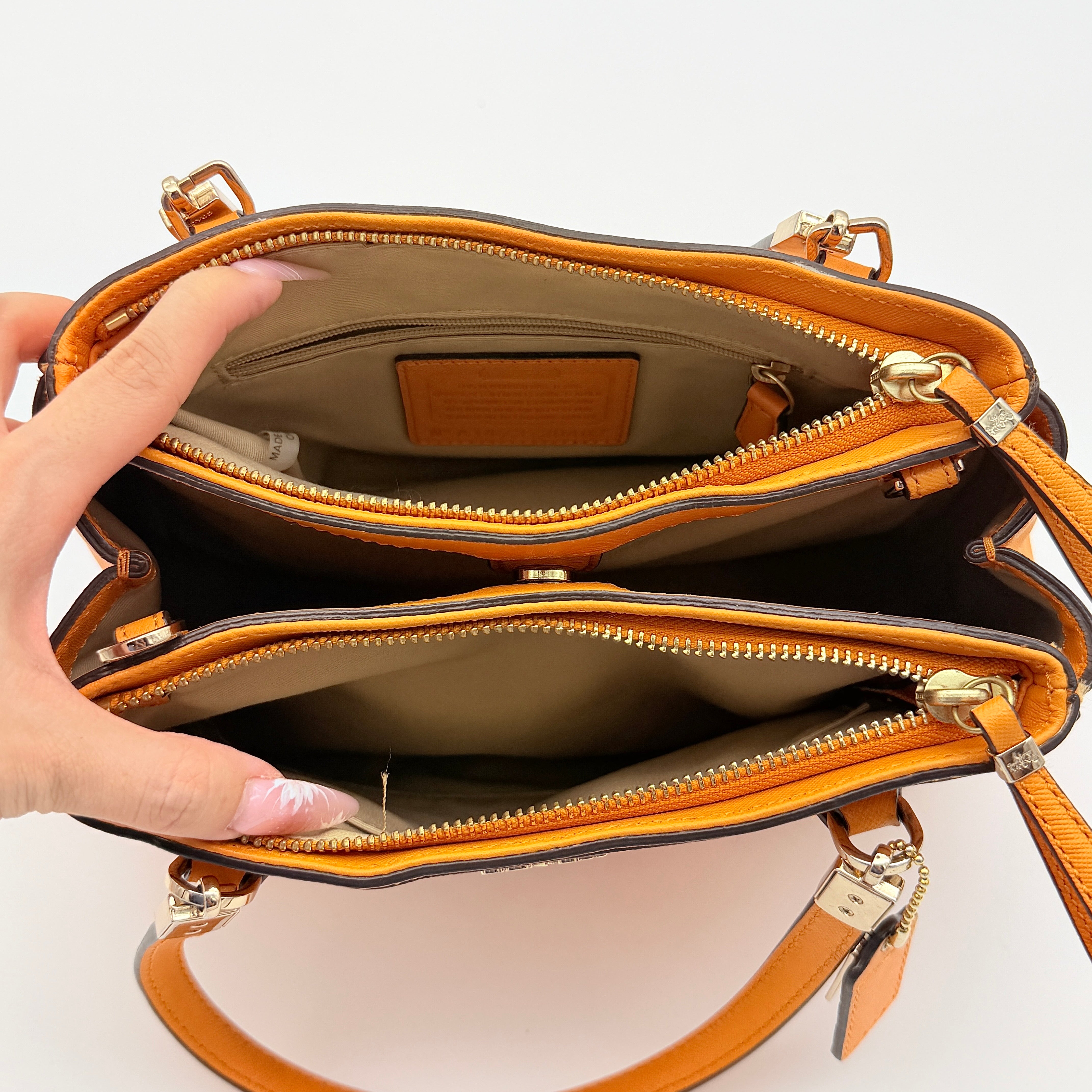 Coach Christie Carryall handbag in orange leather with gold hardware and structured handles, photographed on a white background.