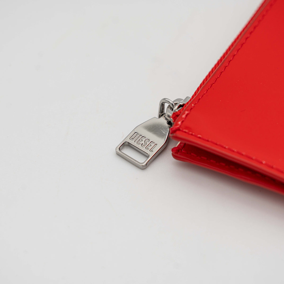 Diesel red patent card holder with silver logo plaque and top zip, set against a clean background.