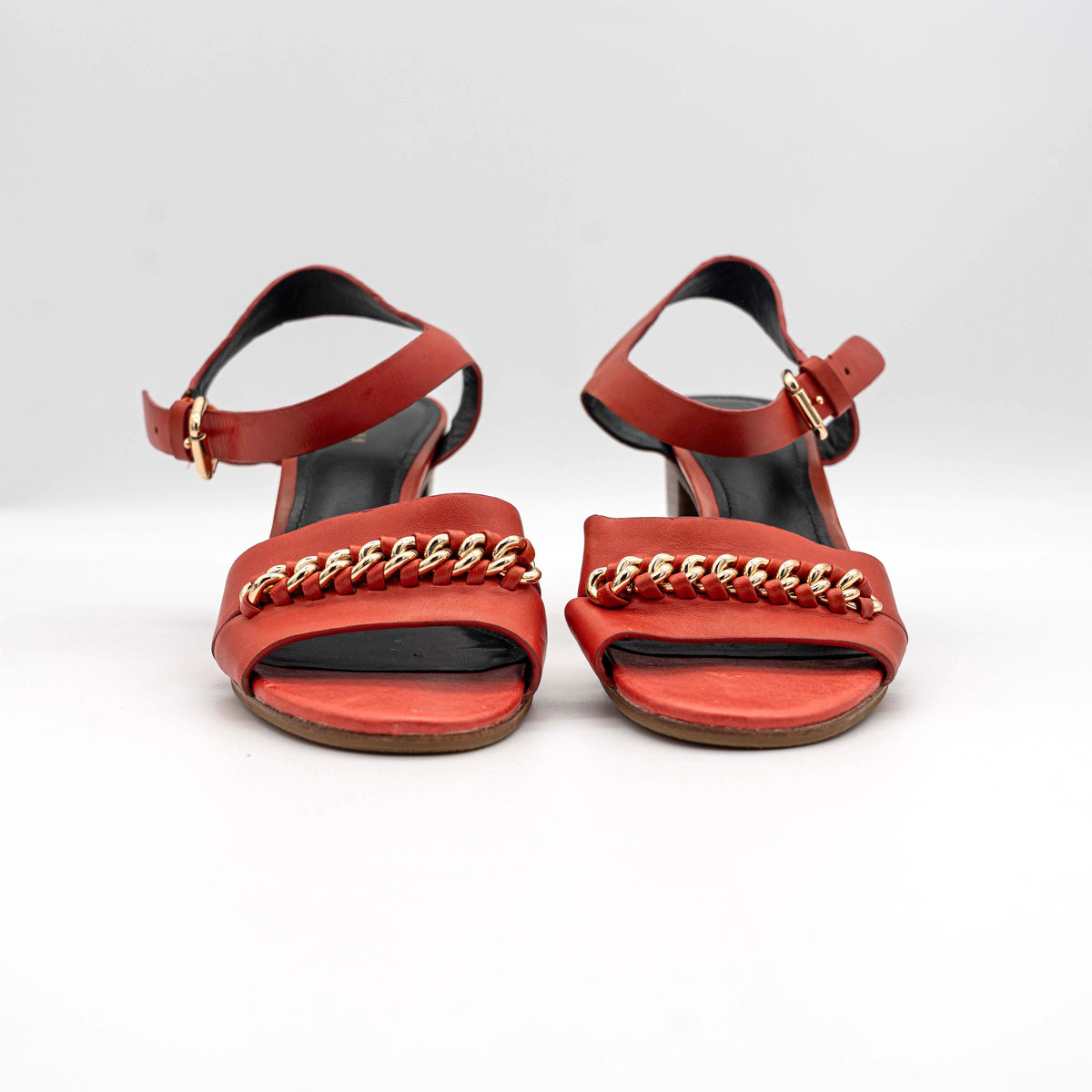 Coach Phoebe block heels in red leather with gold chain detailing, displayed with chunky wood-stacked heels and adjustable ankle straps.