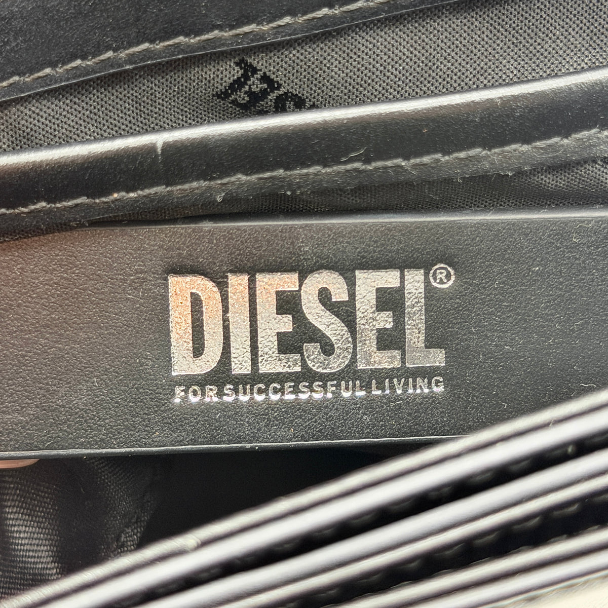 Diesel 1DR Shoulder Bag in black leather with a bold silver and black D logo plaque on the front flap.
