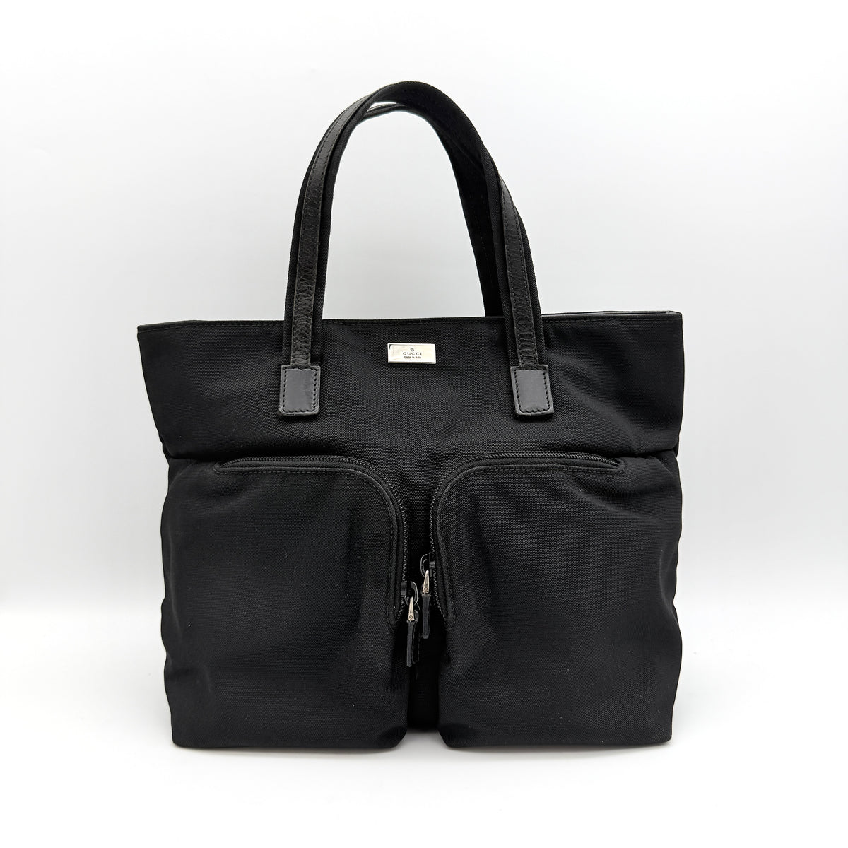 Front view of the Gucci black nylon tote with dual zip pockets and leather top handles.