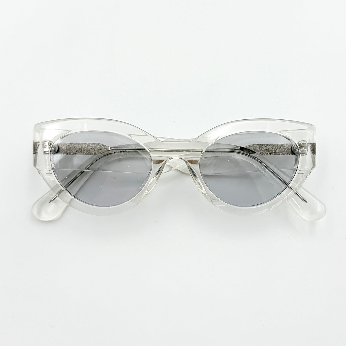Gentle Monster Tazi transparent sunglasses with grey lenses and clear acetate frame, softly styled alongside the branded case.