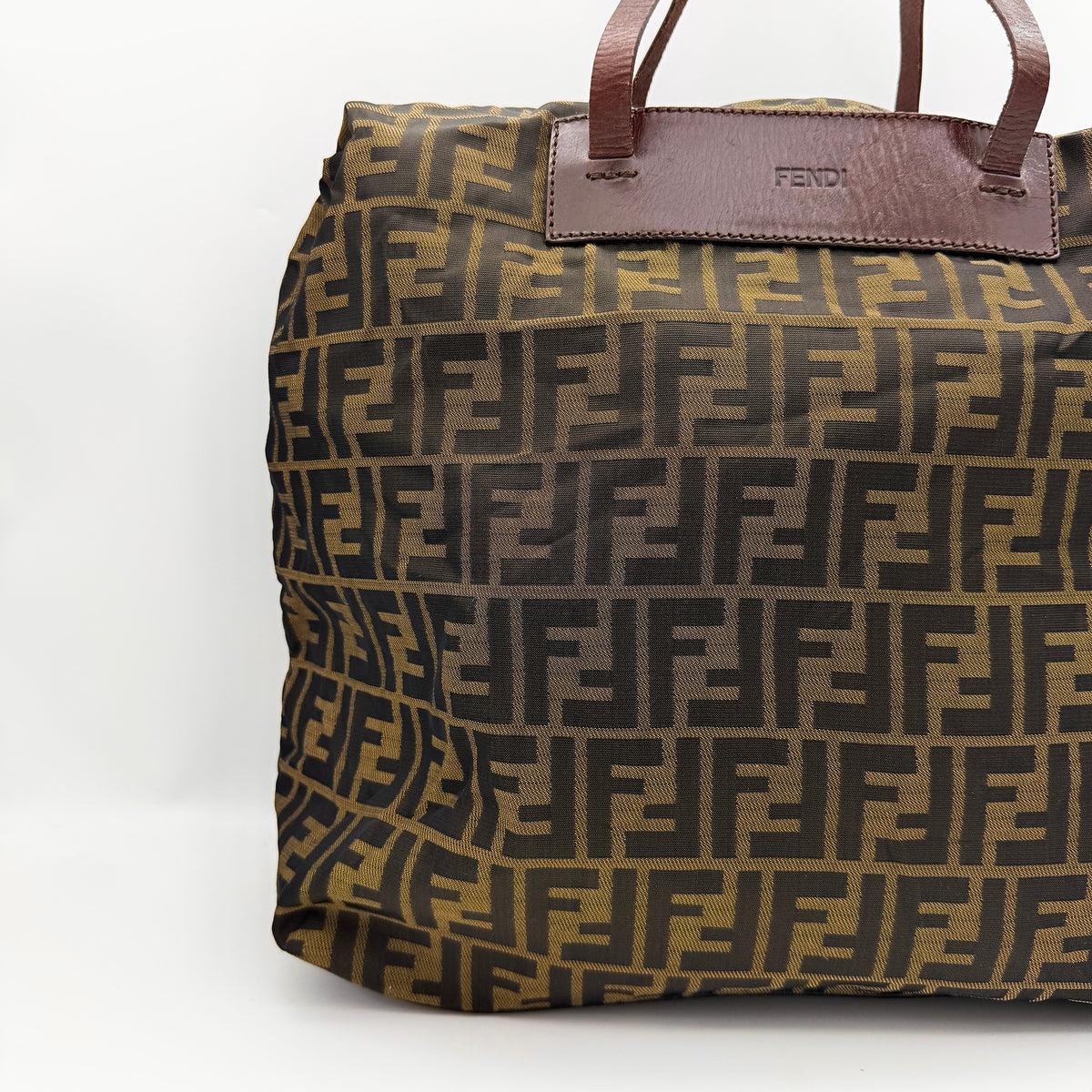 Fendi FF Zucca foldable tote bag in brown canvas with leather top handles and all-over monogram, shown standing upright.