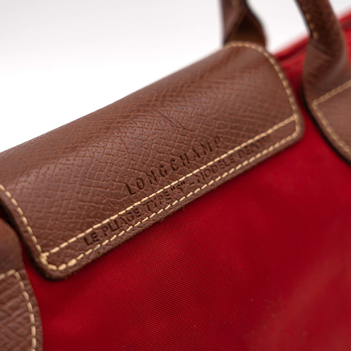 Longchamp Le Pliage handbag in red nylon with brown leather handles and gold-tone accents, photographed on a white background.