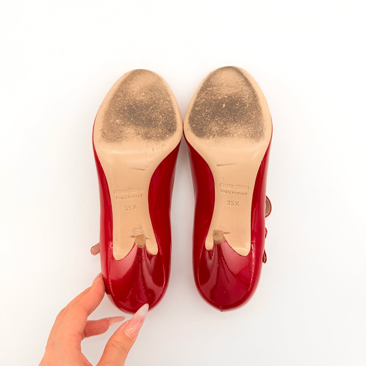 A pair of red patent leather Miu Miu Mary Jane heels with adjustable buckle straps and high heels, displayed against a white background.