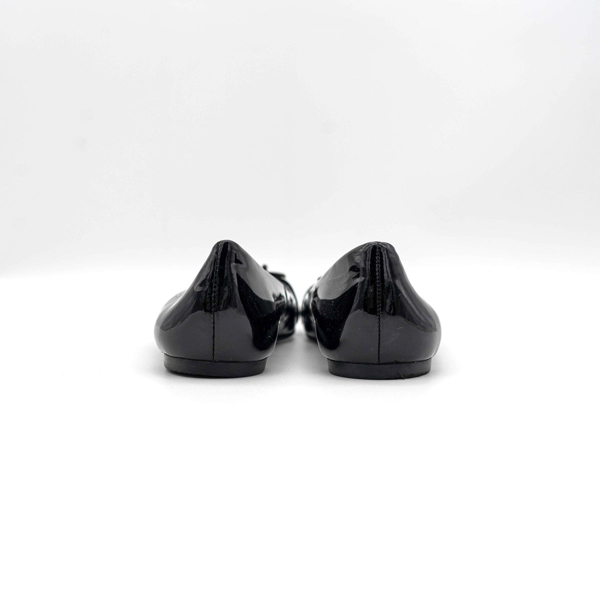 Coach Oswald Turnlock black patent leather ballet flats with dark metal hardware on the toe, photographed on a white background.