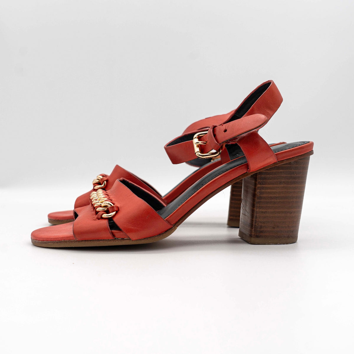 Coach Phoebe block heels in red leather with gold chain detailing, displayed with chunky wood-stacked heels and adjustable ankle straps.