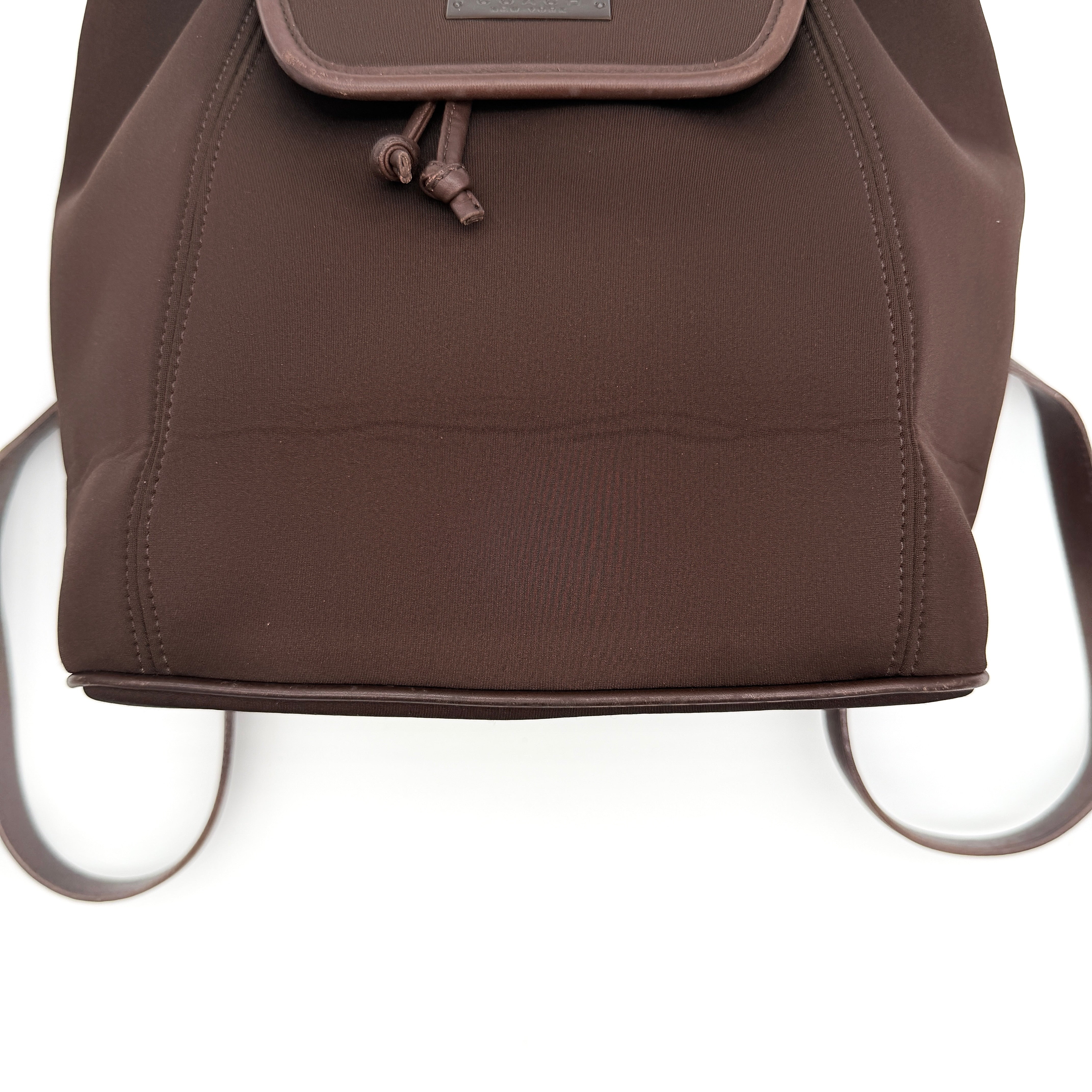 Coach brown neoprene drawstring backpack with leather trim, silver-tone hardware, and adjustable straps shown against a white background.
