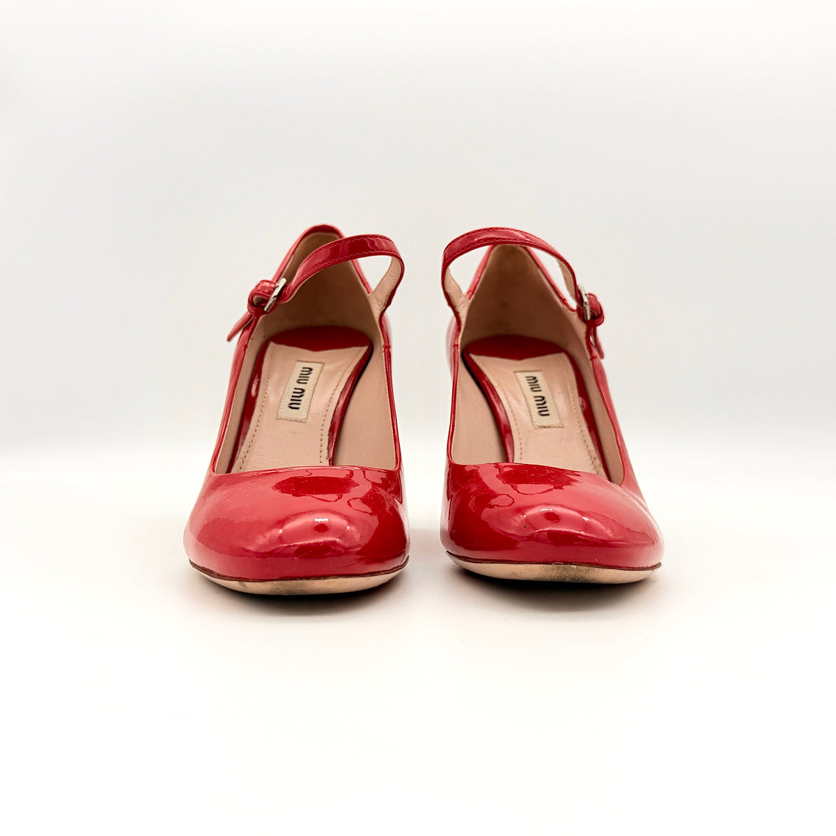 A pair of red patent leather Miu Miu Mary Jane heels with adjustable buckle straps and high heels, displayed against a white background.