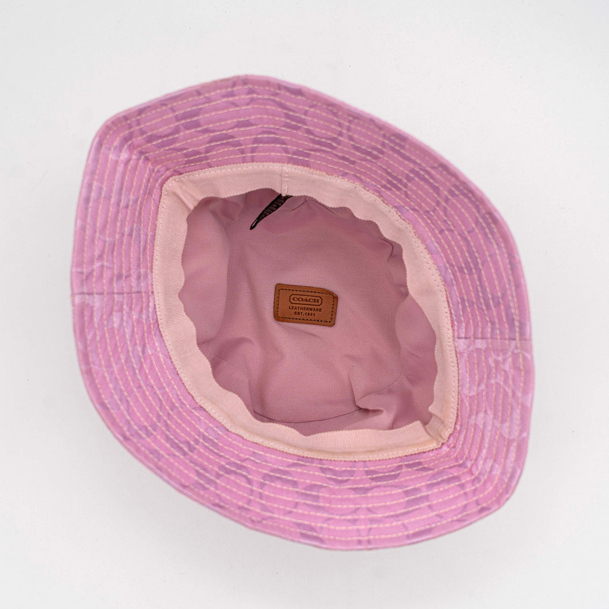 Coach pink jacquard bucket hat with taupe suede-effect band, shown against a neutral background.
