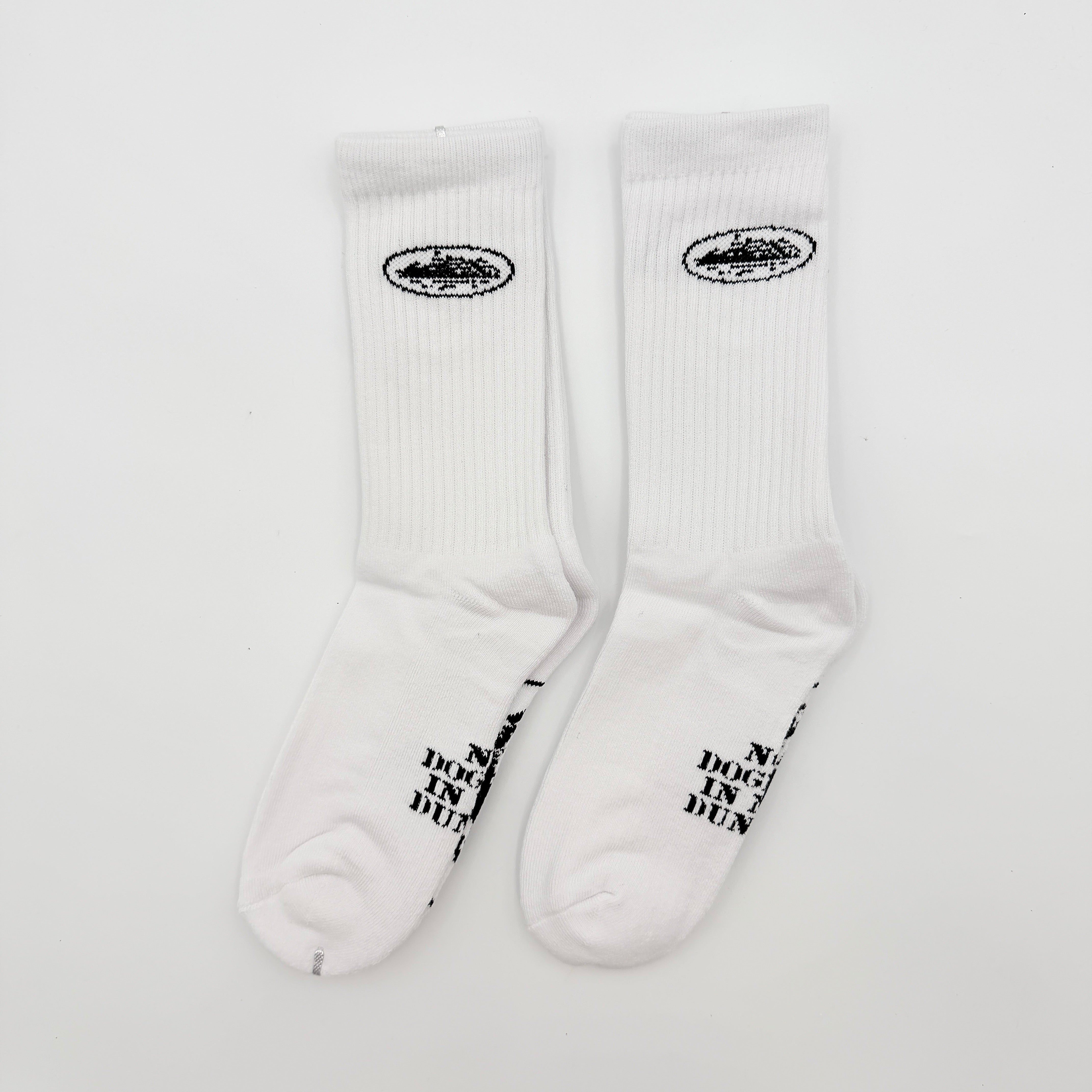 A pair of Corteiz Alcatraz white socks with black logo on the ankle and statement text on the sole.