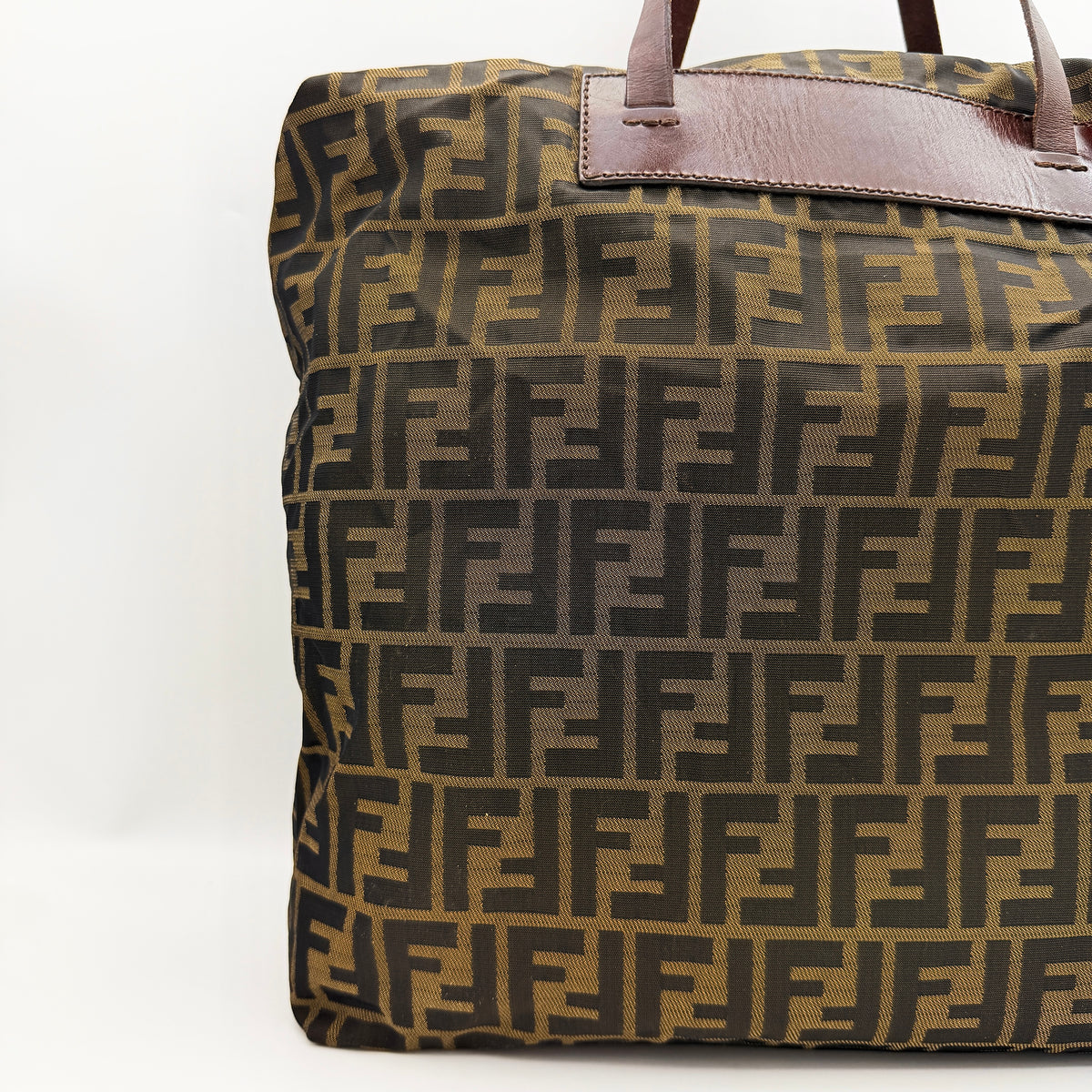 Fendi FF Zucca foldable tote bag in brown canvas with leather top handles and all-over monogram, shown standing upright.