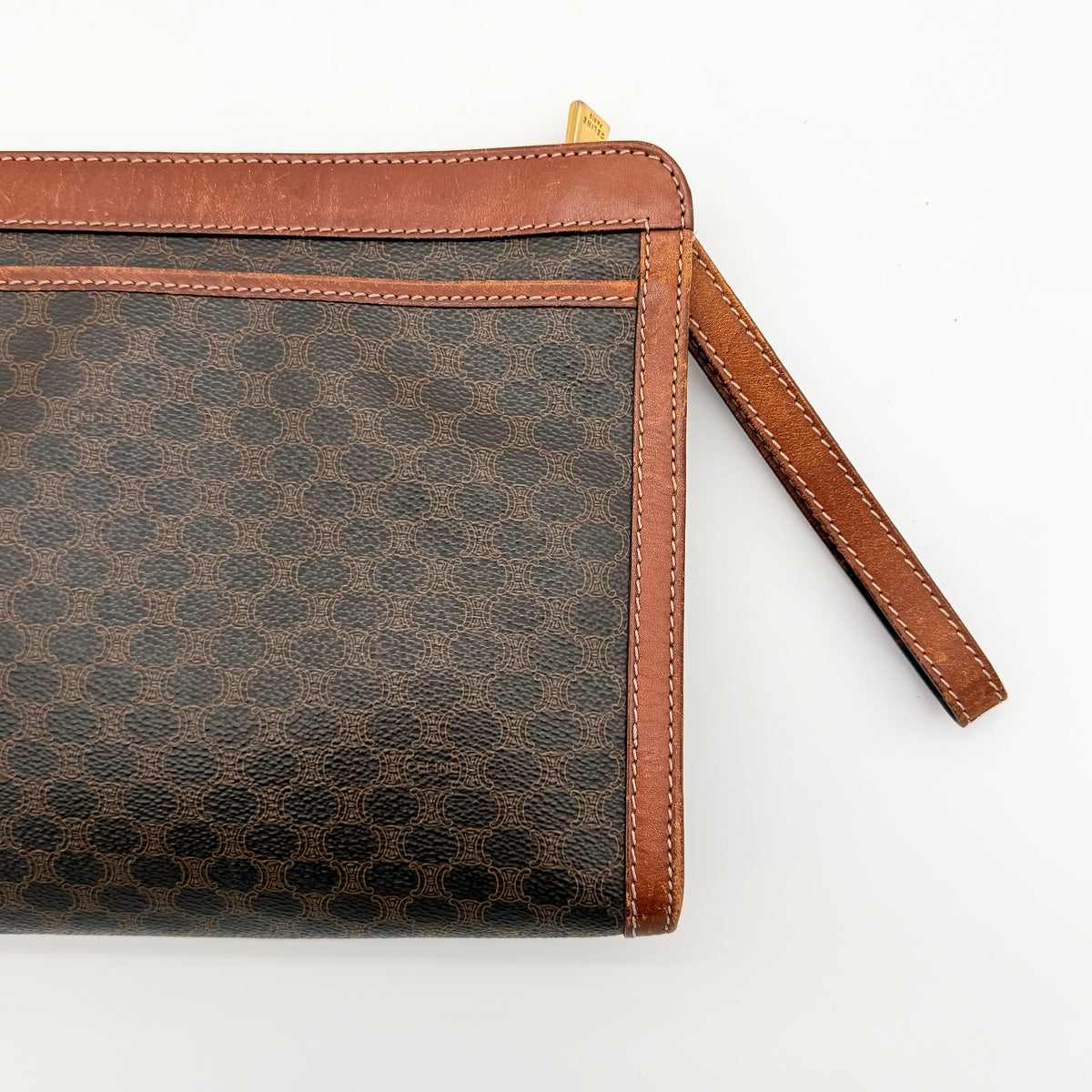 Celine Triomphe Macadam clutch bag in brown canvas with tan leather trim and gold hardware, shown with wrist strap.