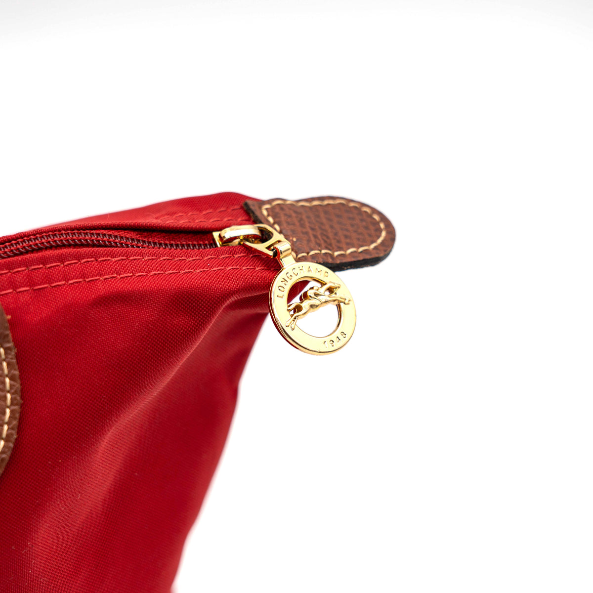 Longchamp Le Pliage handbag in red nylon with brown leather handles and gold-tone accents, photographed on a white background.