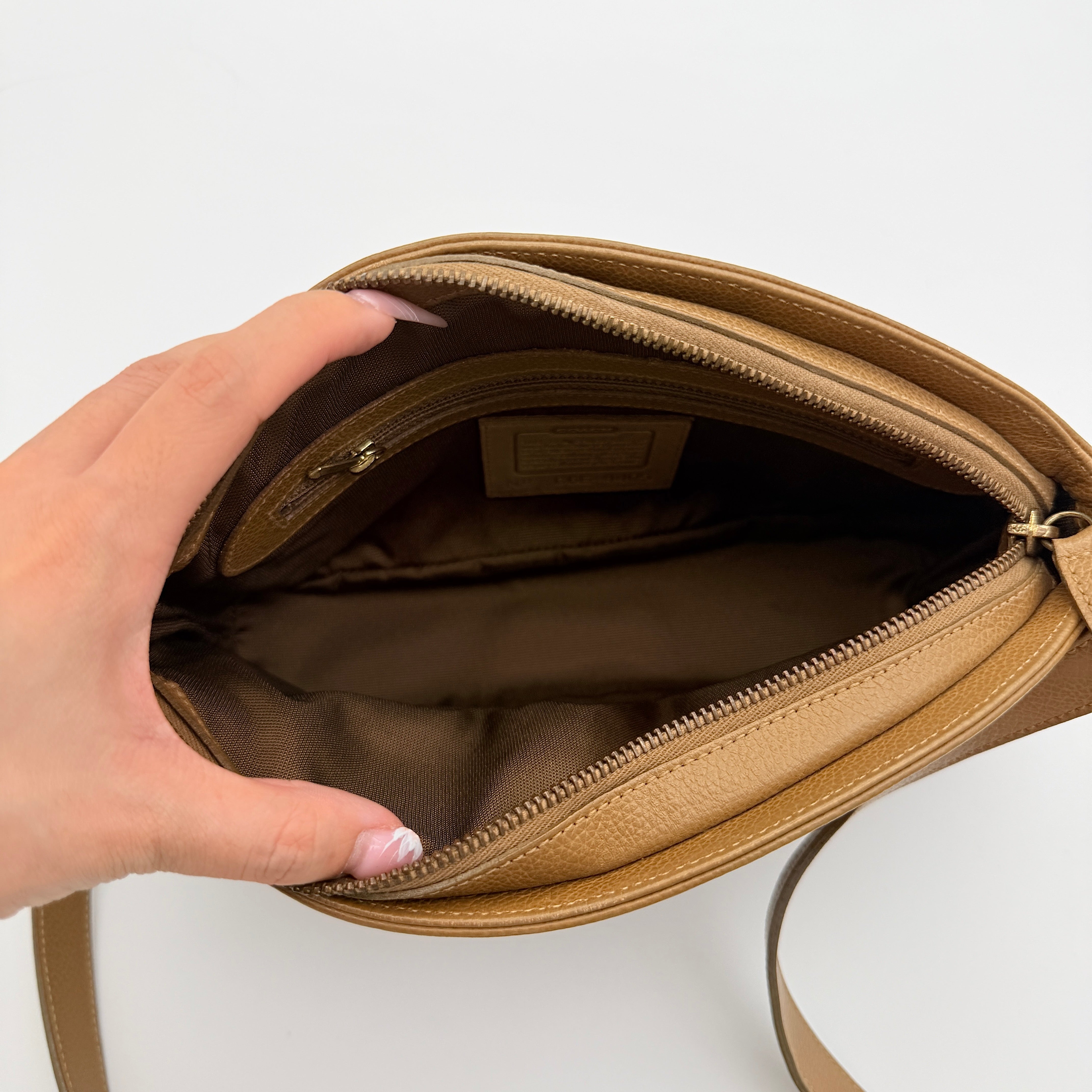 Coach tan leather crossbody bag with gold-tone hardware and adjustable strap, photographed on a white background.