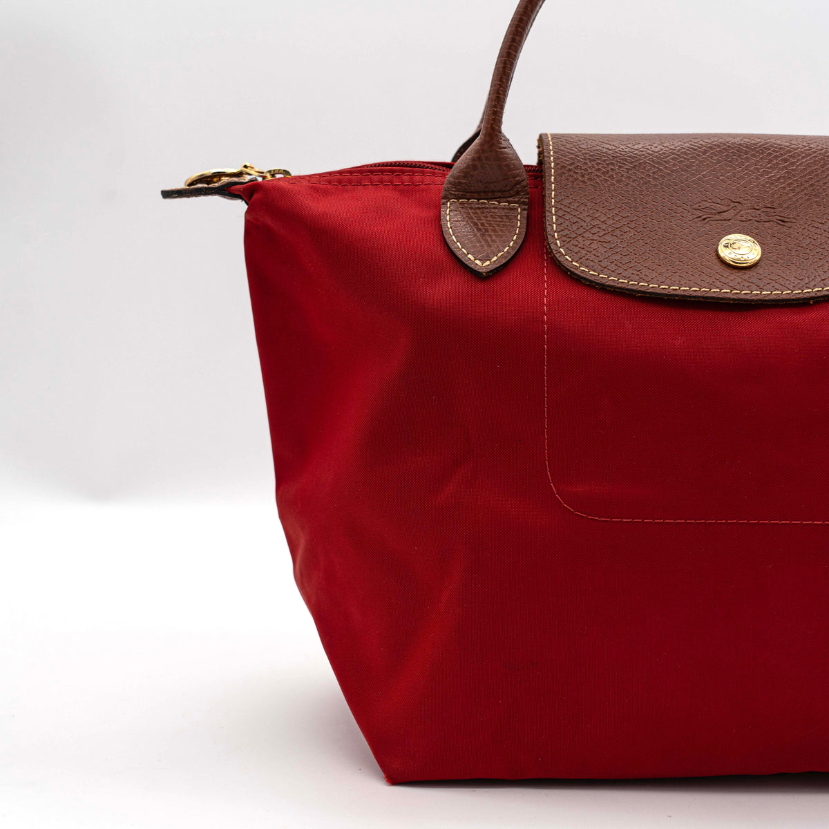 Longchamp Le Pliage handbag in red nylon with brown leather handles and gold-tone accents, photographed on a white background.