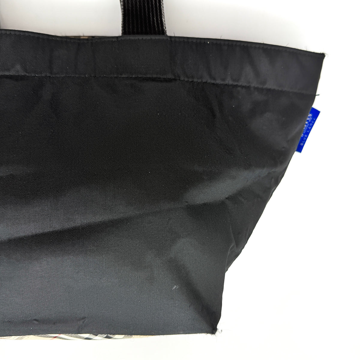 Burberry Blue Label Nova Check tote bag in black nylon with beige checked base and webbed handles, shown on white background.