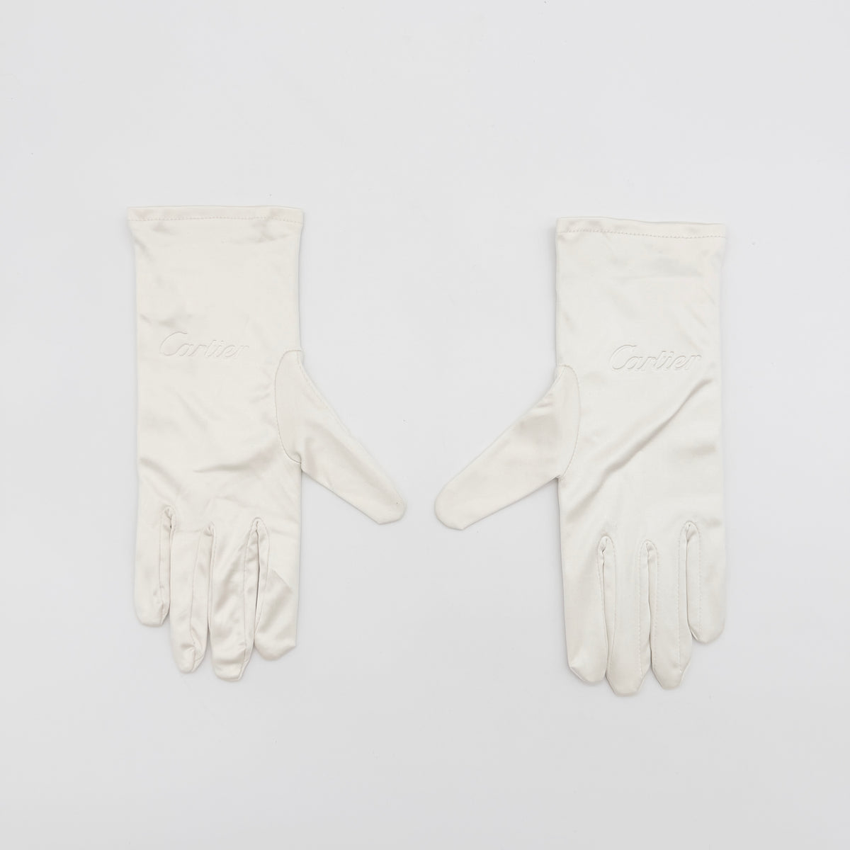 Pair of Cartier ivory gloves with signature script logo embroidery displayed on a flat white background.