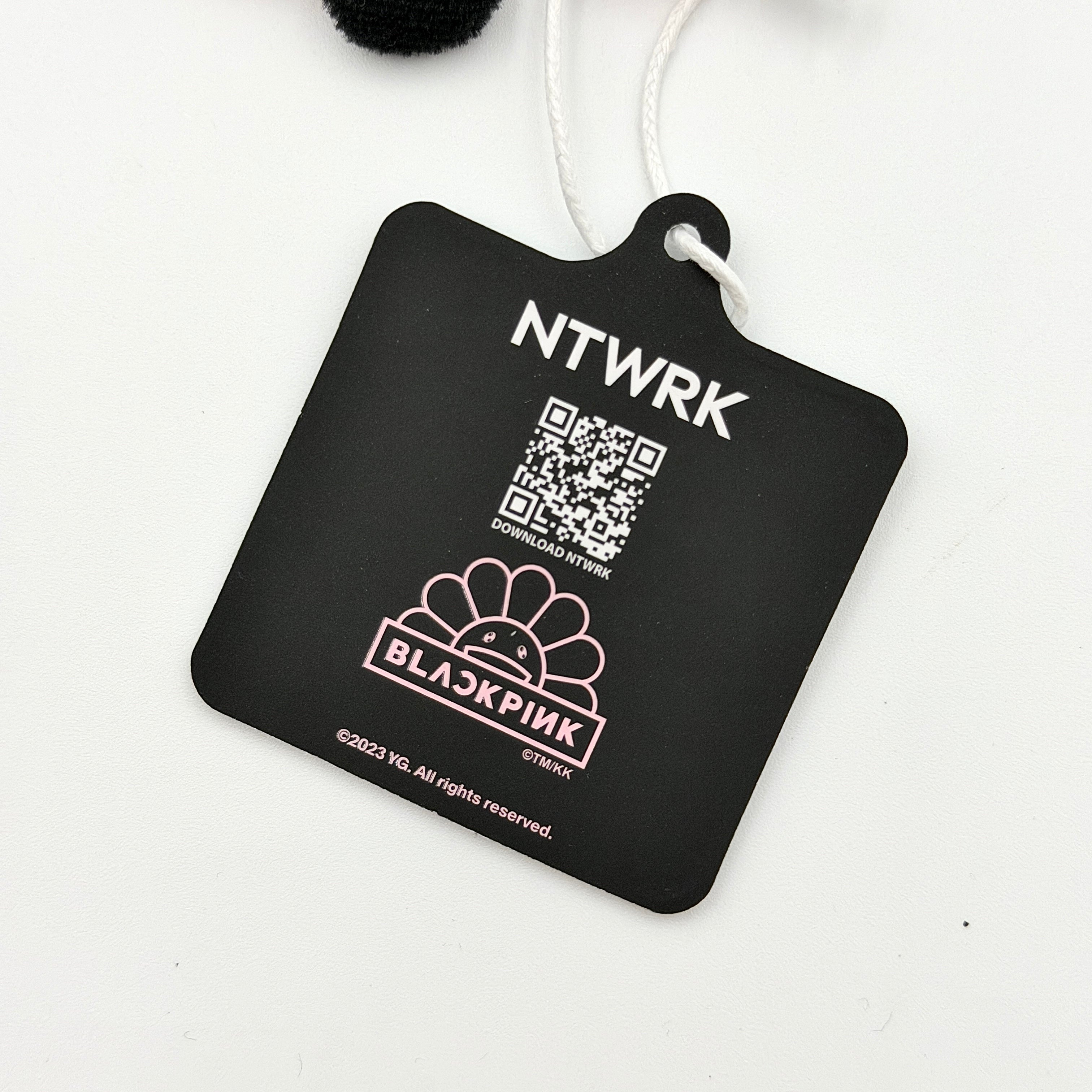 Takashi Murakami x BLACKPINK plush flower keychain in black and pink with smiling face and branded tag.