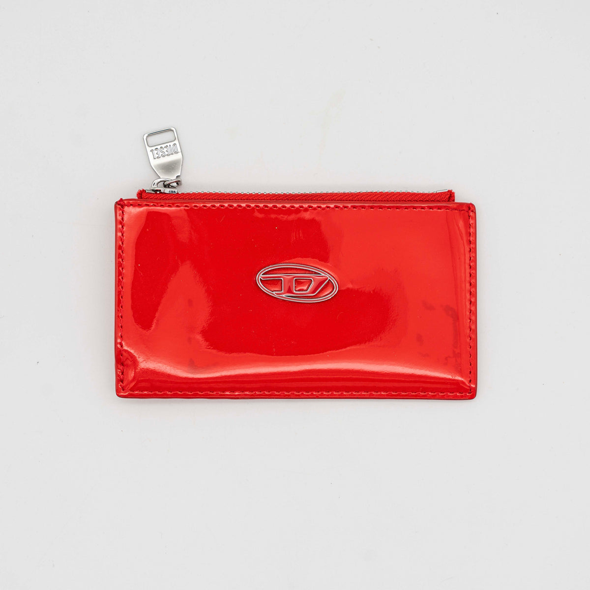 Diesel red patent card holder with silver logo plaque and top zip, set against a clean background.