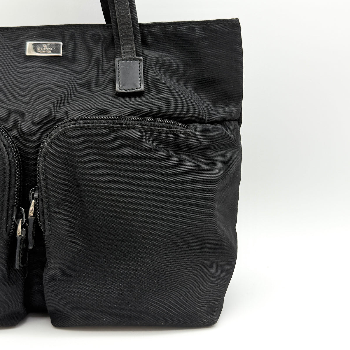 Front view of the Gucci black nylon tote with dual zip pockets and leather top handles.