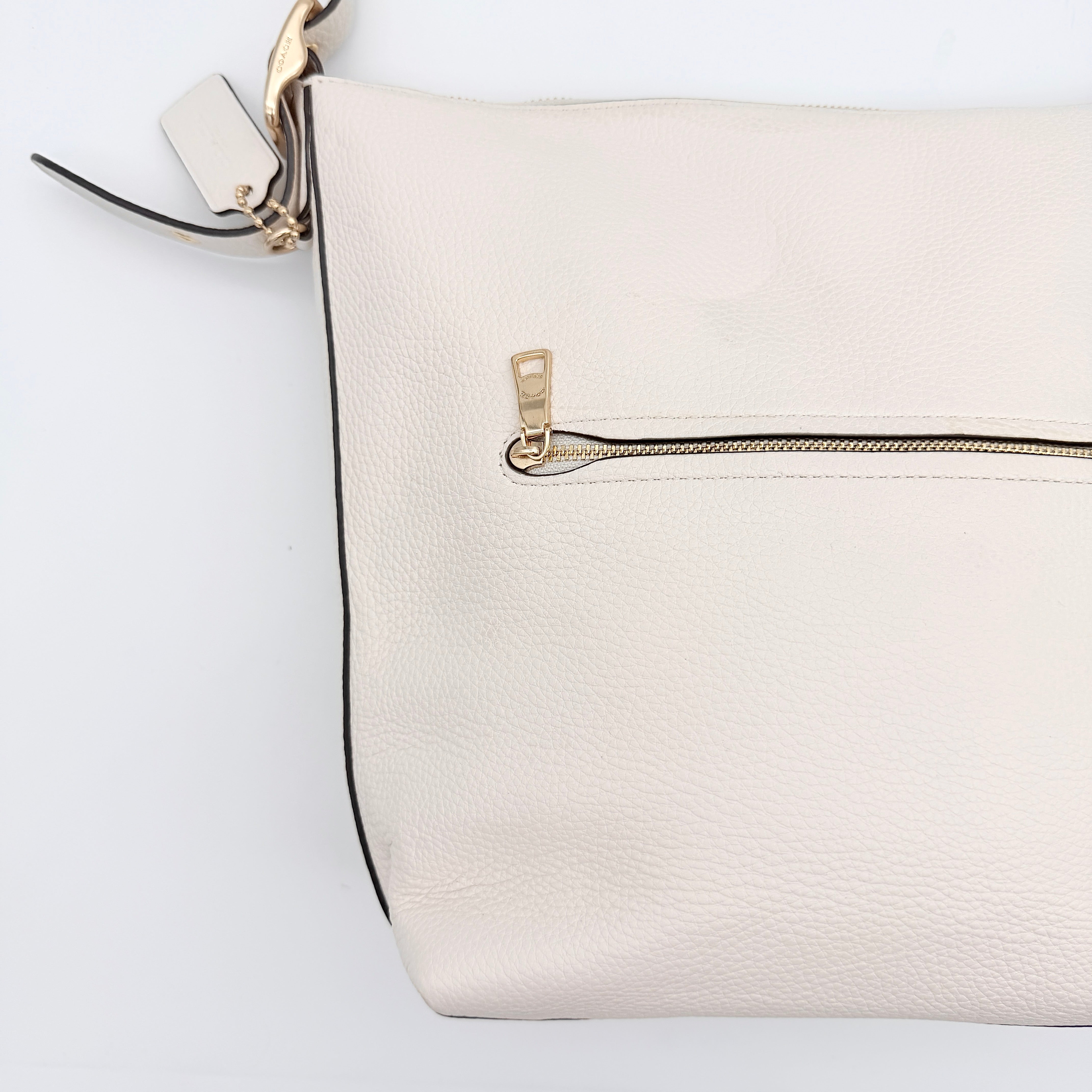 Coach Ellie File Crossbody Bag in ivory pebbled leather with gold hardware and adjustable strap, displayed on a white background.