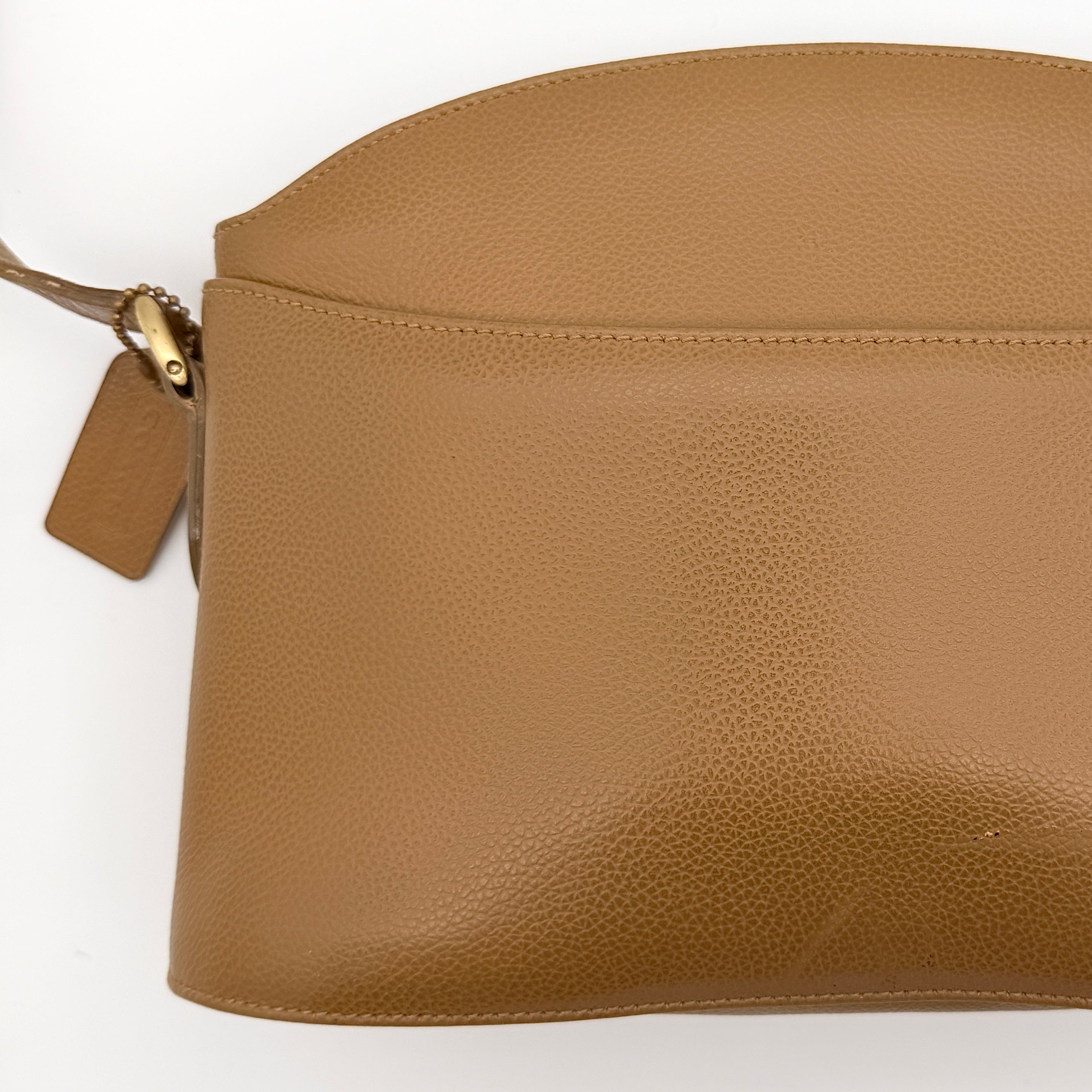 Coach tan leather crossbody bag with gold-tone hardware and adjustable strap, photographed on a white background.
