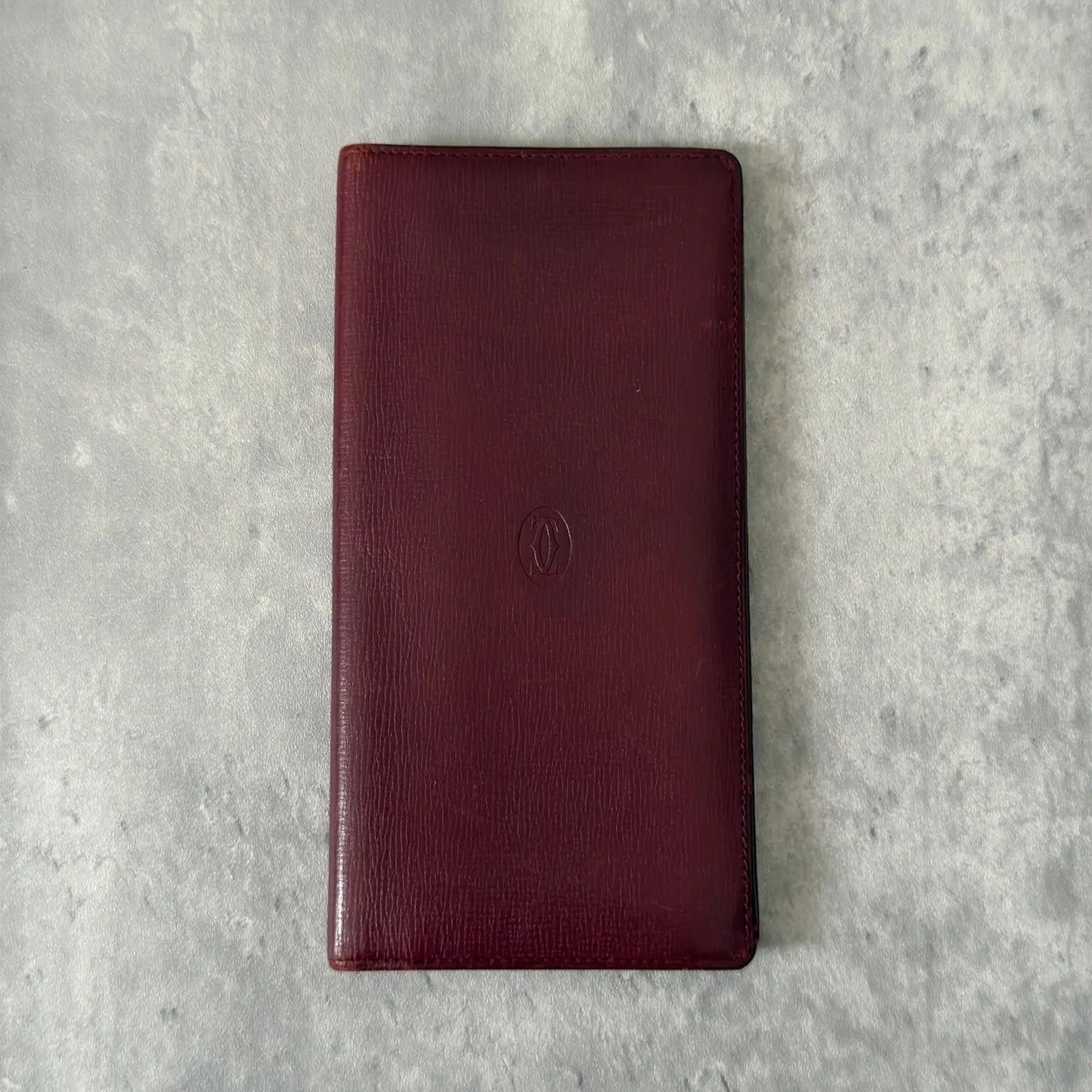 Cartier Must de Cartier Bifold Long Wallet in rich burgundy leather, detailed with multiple card slots, bill compartments, and a discreet embossed logo on the front cover.
