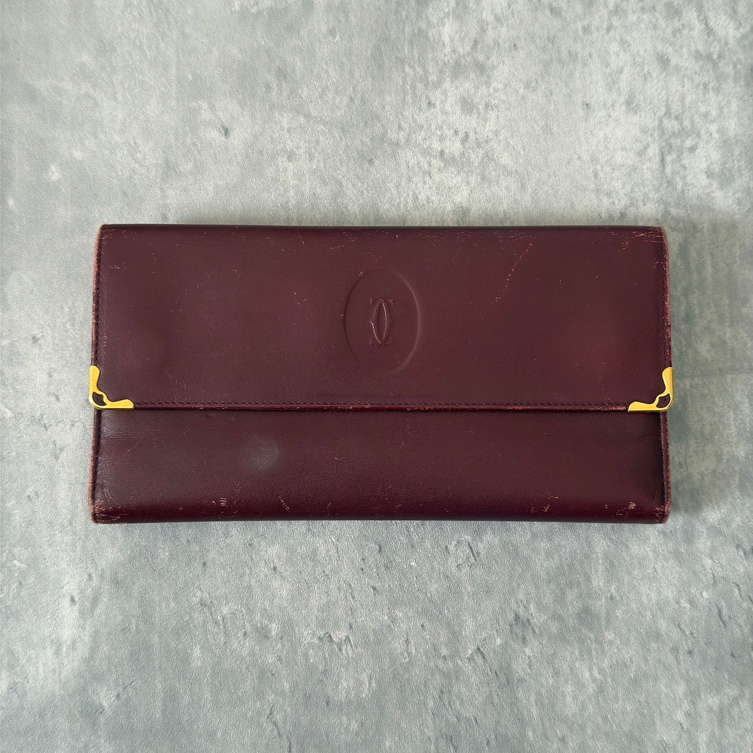 Cartier Must de Cartier trifold continental wallet in burgundy leather, showcasing detailed craftsmanship, gold-tone Cartier logo, and an organized interior.