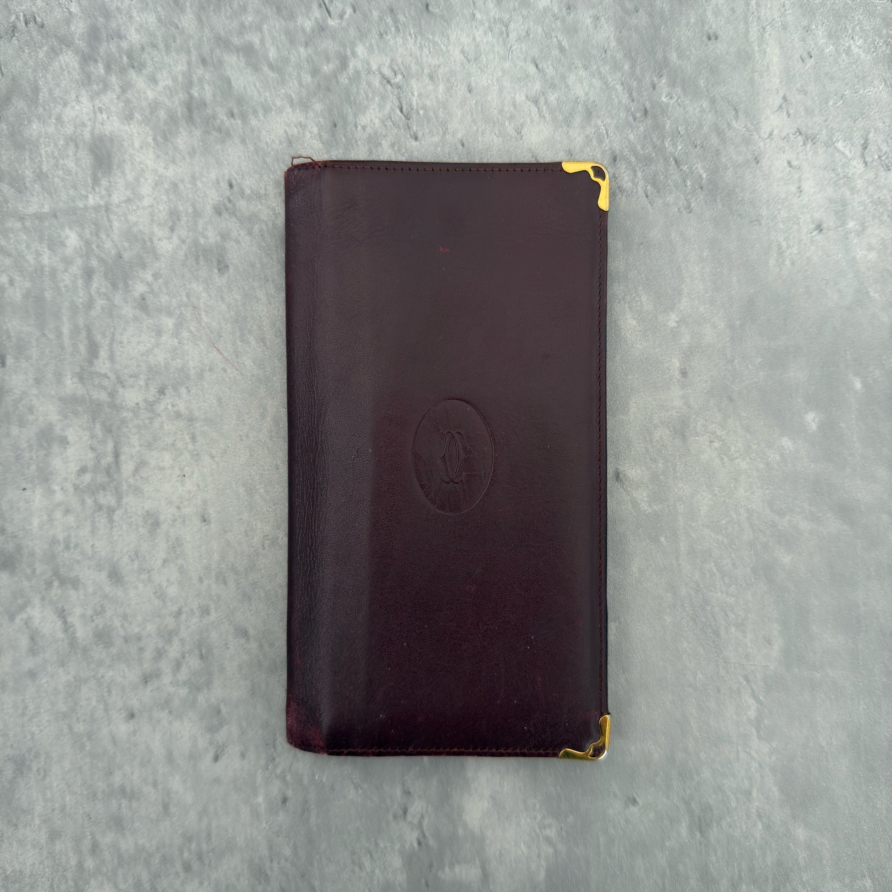 Cartier Must De Cartier Burgundy Long Wallet in burgundy leather with gold-tone corner accents and multiple compartments.