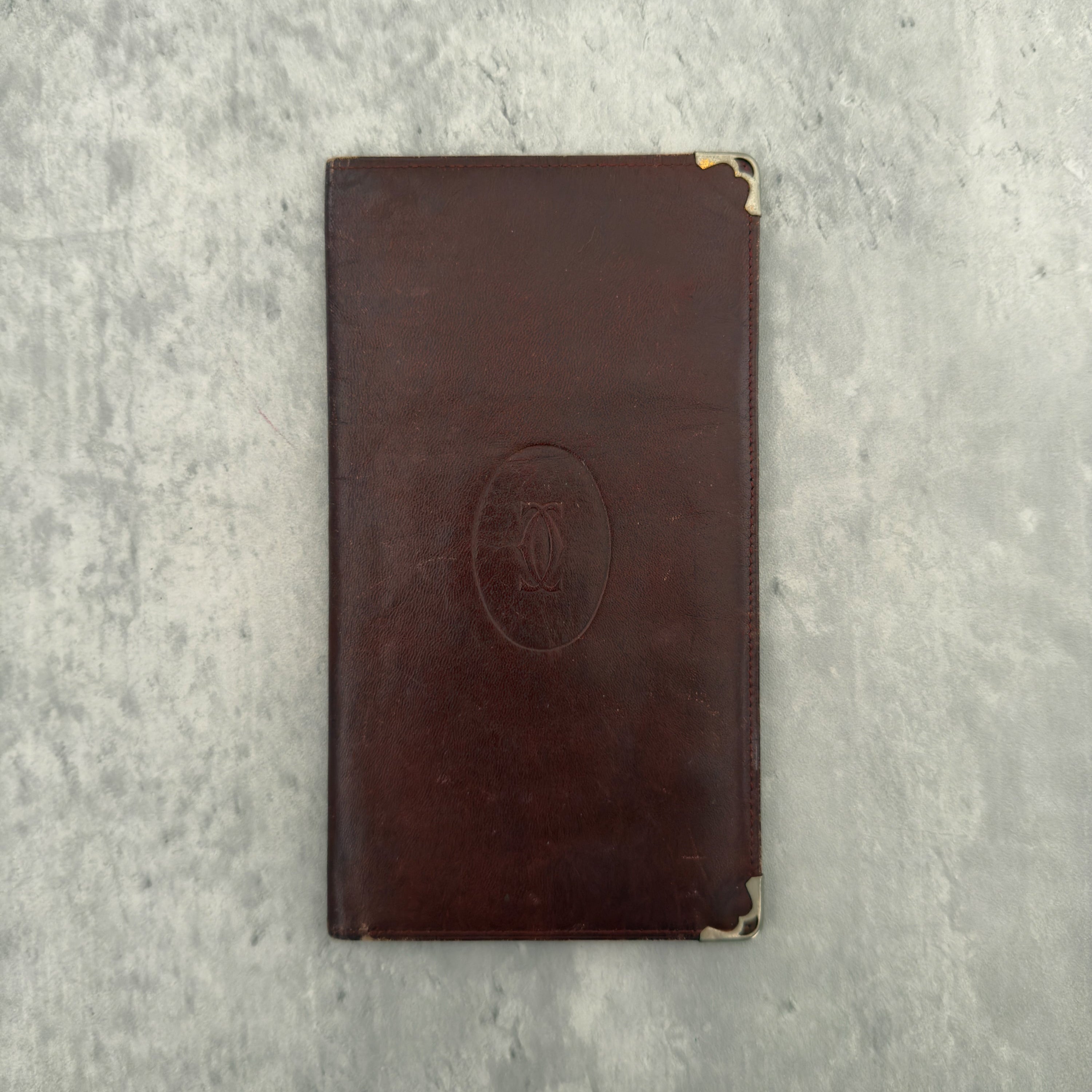 Cartier Must De Cartier Long Wallet in burgundy leather with embossed logo, gold-tone corner accents, and multiple compartments for organised storage.