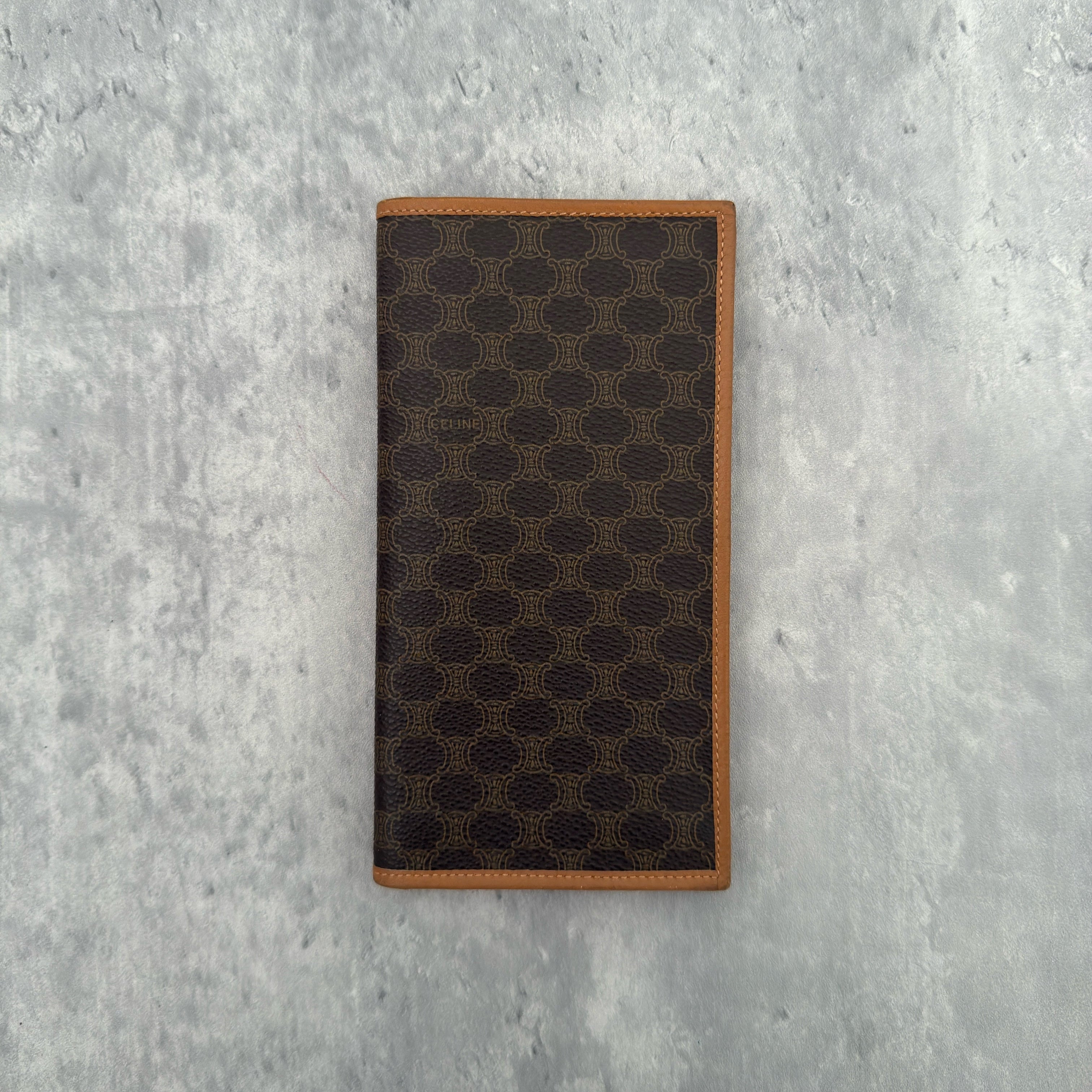 Celine Macadam Triomphe Canvas Long Wallet in brown monogram canvas with tan leather trim, featuring a bifold design with multiple compartments and a snap-button coin pocket.