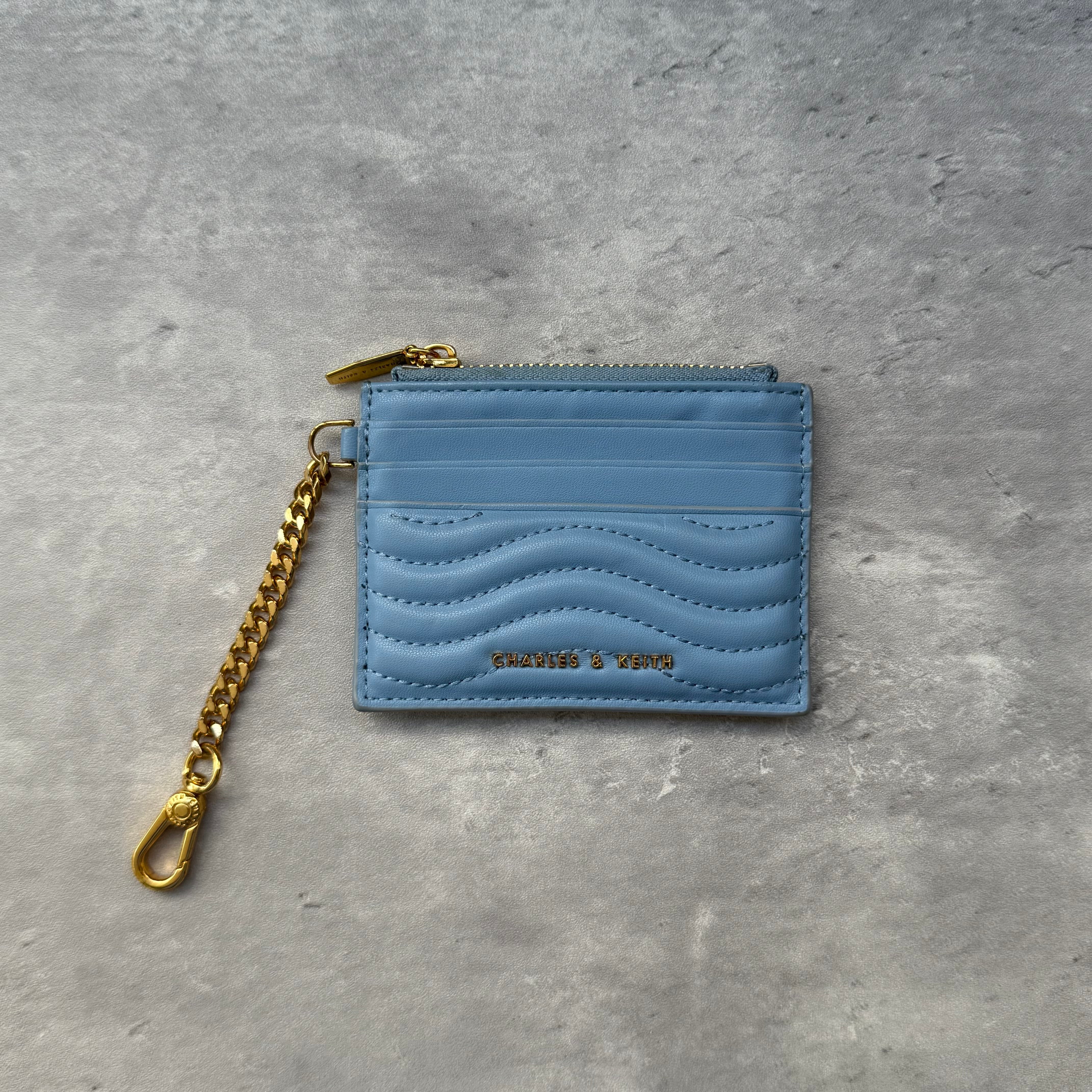 Charles & Keith Aubrielle Stitch-Trim Zip Cardholder in light blue faux leather with wave stitch detailing, zip closure, and gold-tone chain.