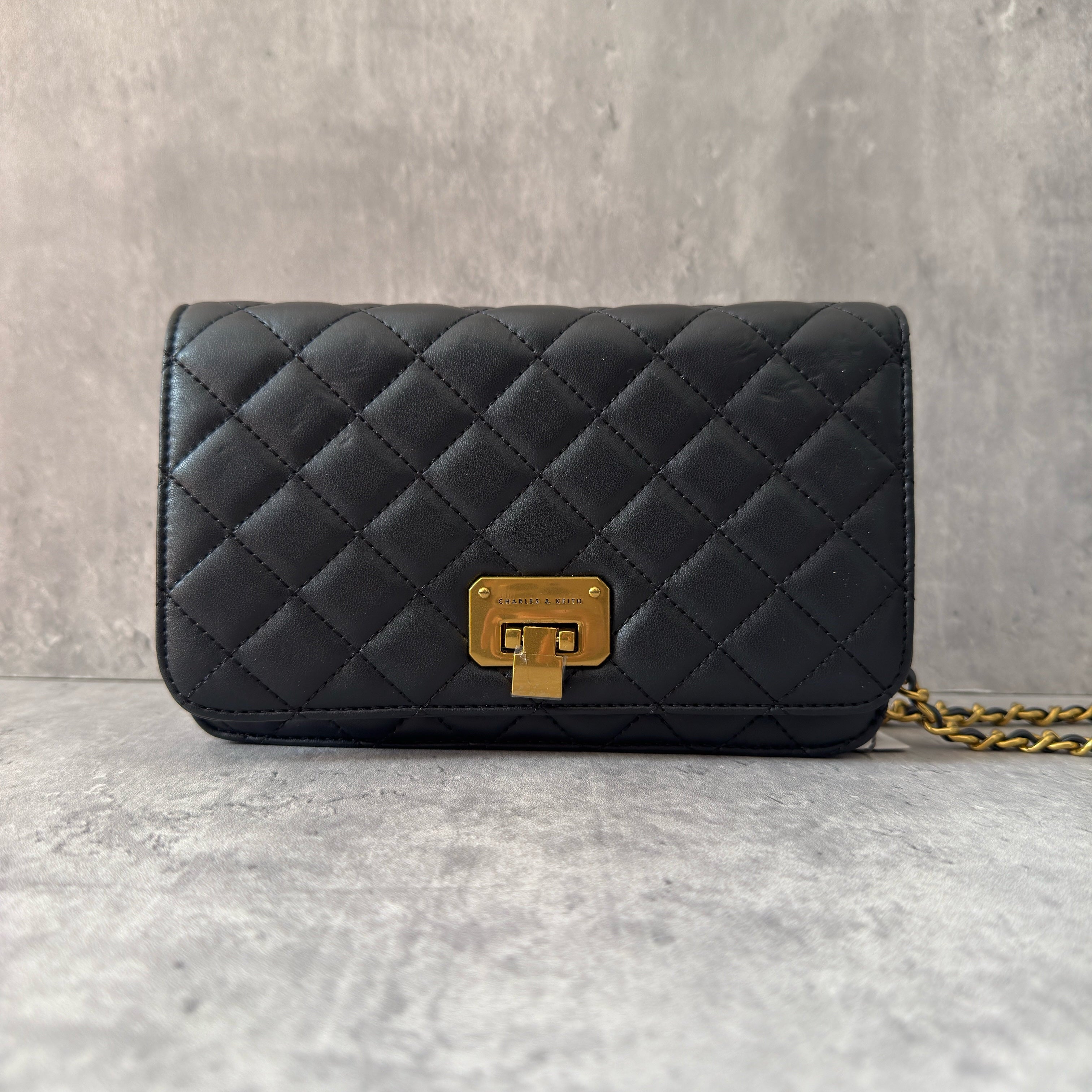 Charles & Keith Cressida Quilted Push-Lock Clutch Bag in black faux leather with gold-tone chain strap and secure push-lock closure.