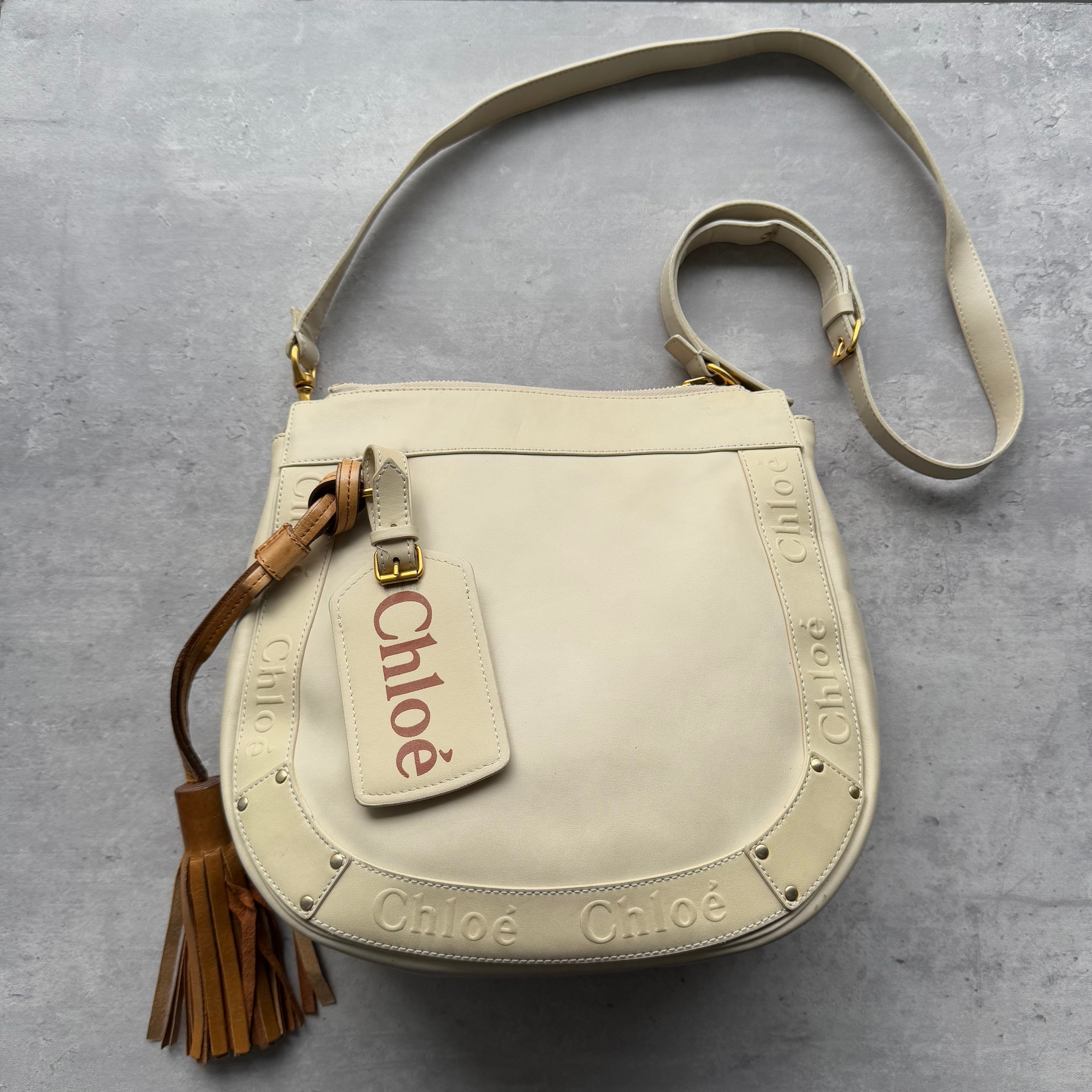 Chloé Eden Crossbody Bag in cream leather with embossed logo trim, tassel detail, gold hardware, and red fabric interior.