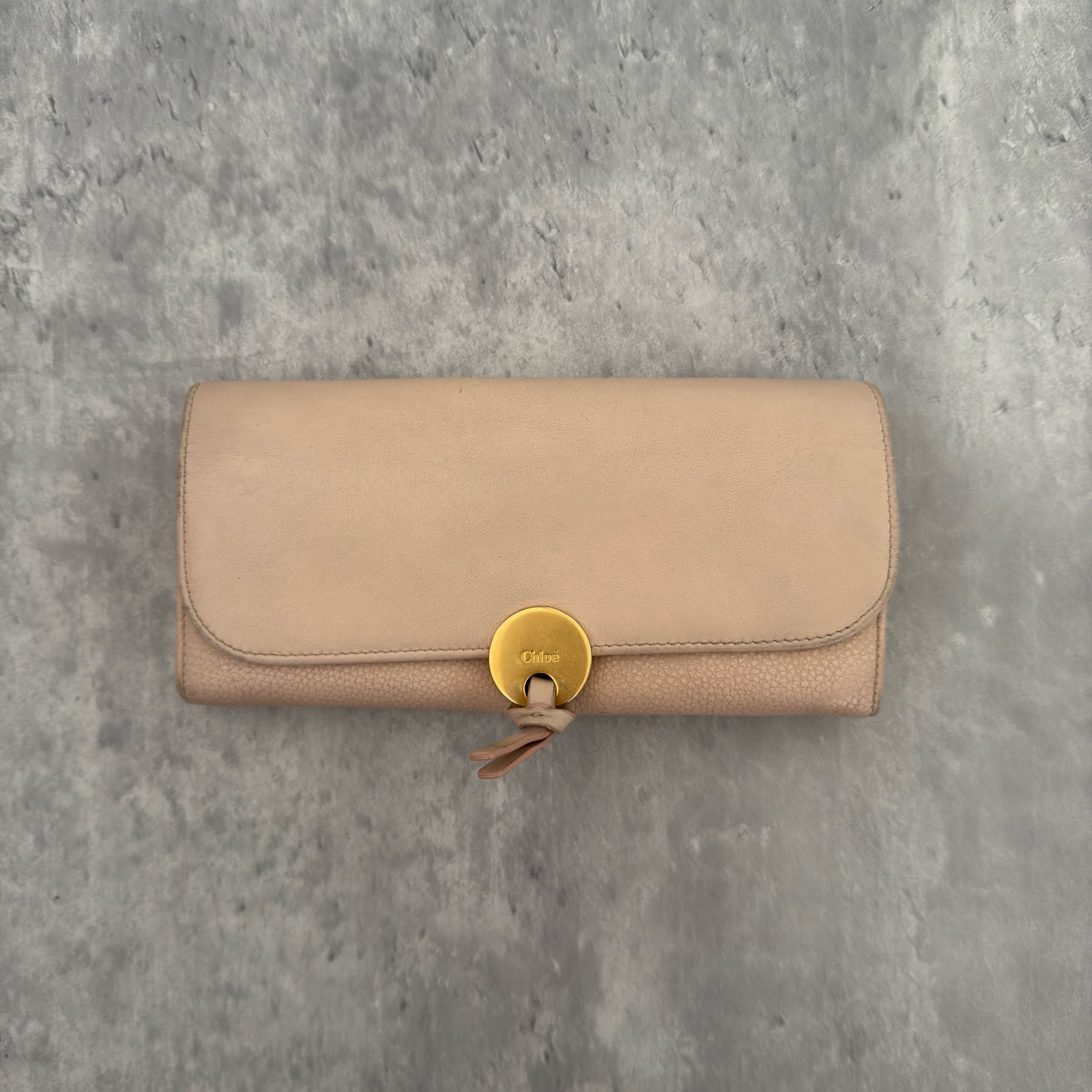 Chloe Grained Smooth Calfskin Indy Long Wallet in Light Pink, featuring a gold-tone circular medallion closure with leather tie detail, crafted from a mix of grained and smooth calfskin leather.