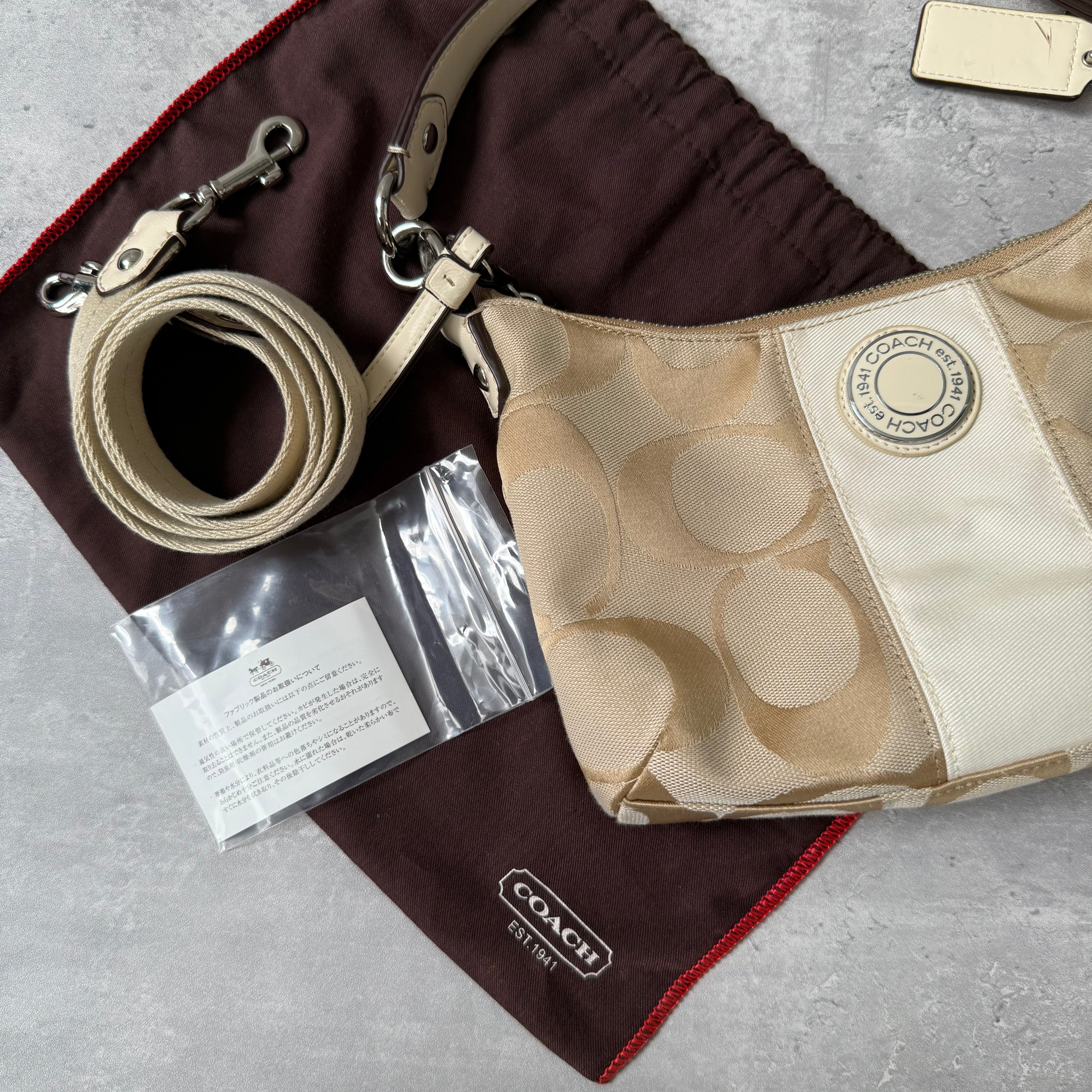 Coach 2-Way Signature Stripe Shoulder Bag in Beige and White with detachable strap, zip closure, and central white leather stripe with metal Coach emblem