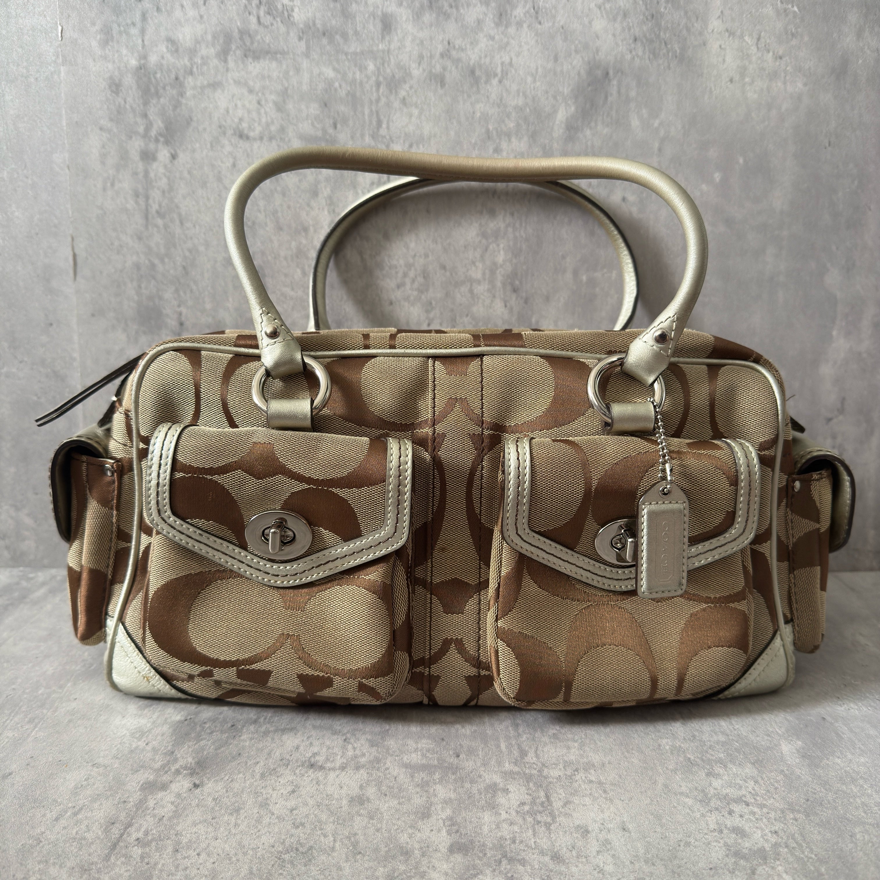 Coach 2Way Poppy Signature Bag in beige monogram canvas with silver leather trim, featuring double handles, turn-lock front pockets, and a spacious interior.