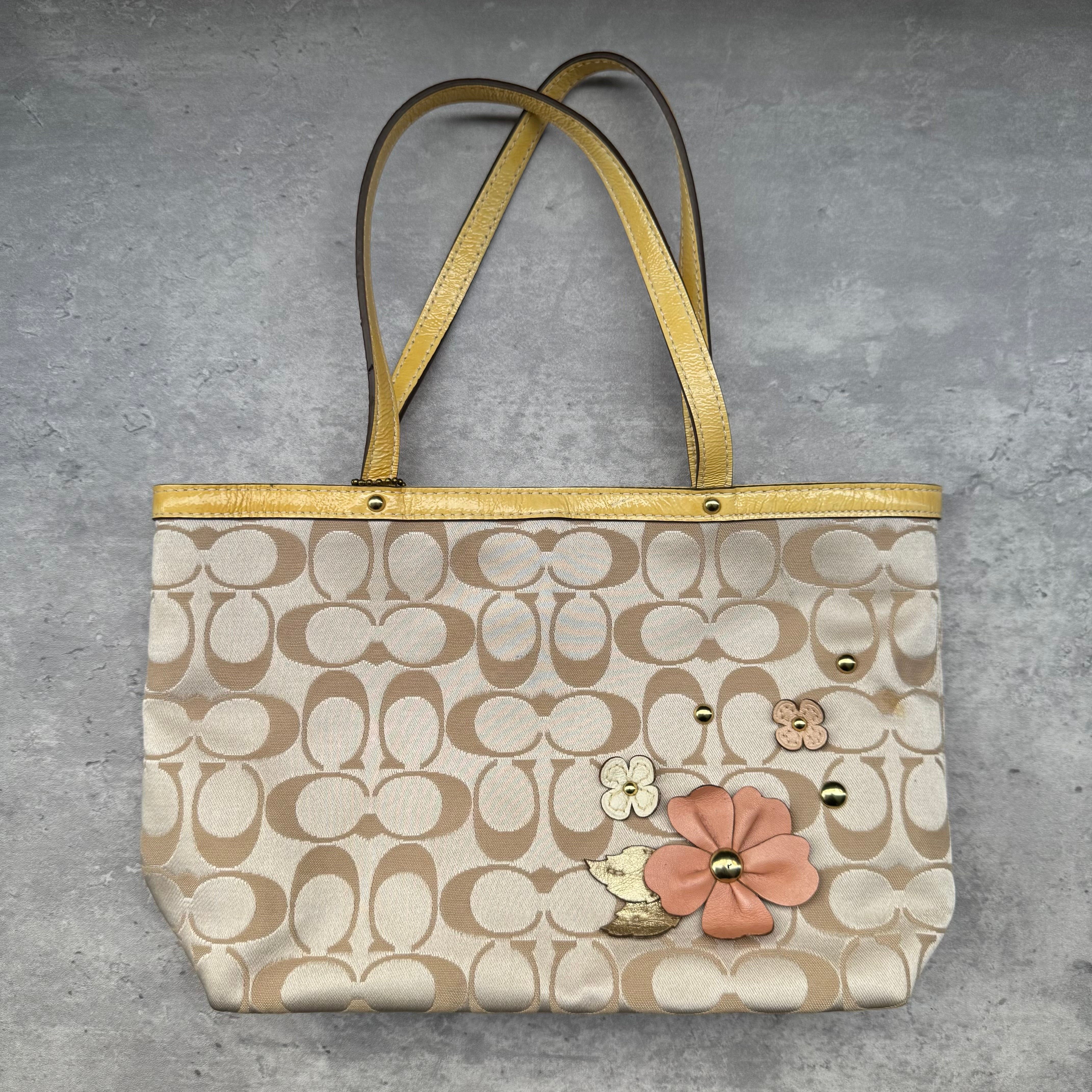 Coach Floral Applique Tote Bag in beige signature canvas with yellow leather trim and pastel leather flower details.