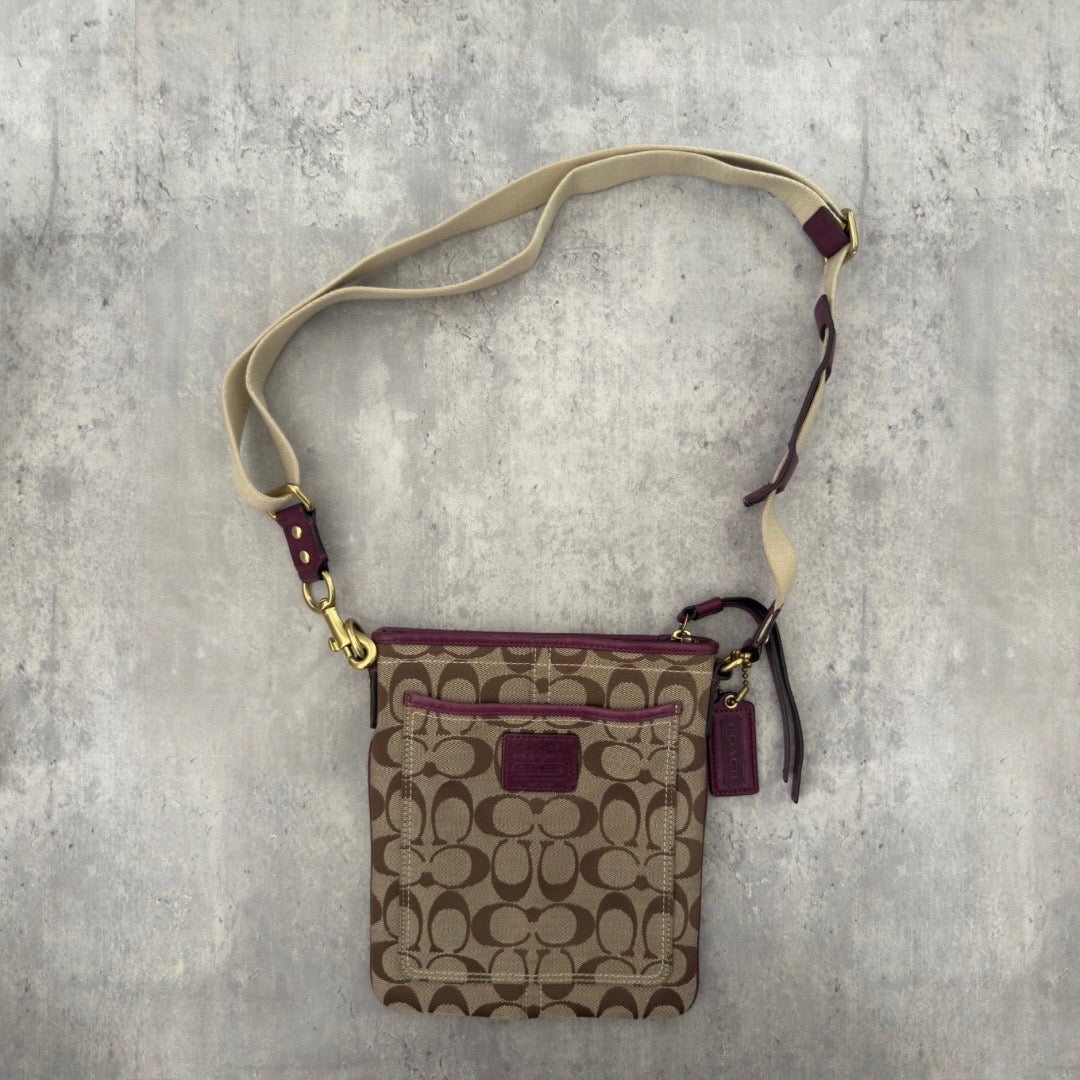 Coach Khaki Signature Crossbody Swing-pack in beige monogram canvas with purple leather trim, featuring an adjustable fabric strap and zippered top closure.