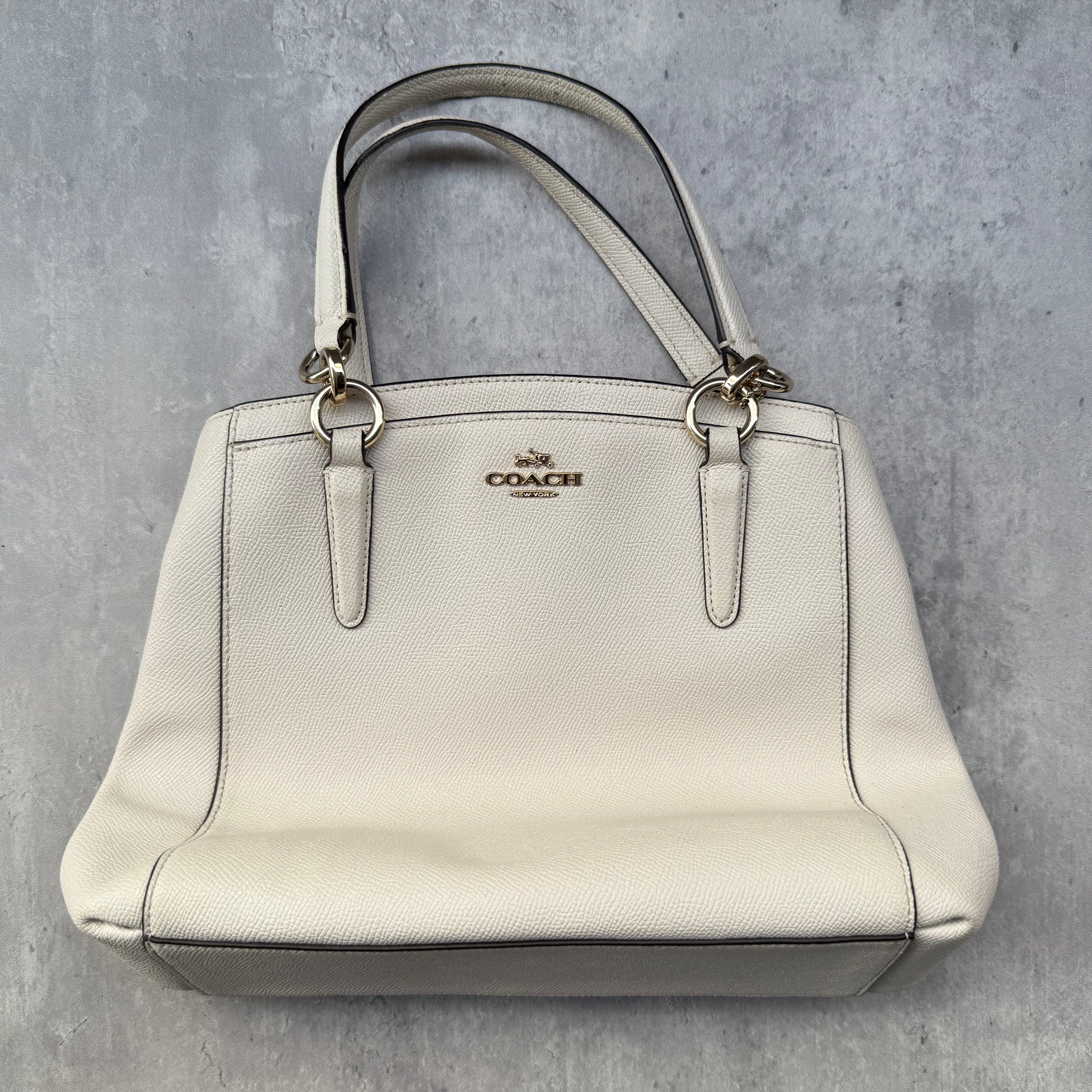 Coach Minetta Handbag in white pebbled leather with structured silhouette, top handles, and gold-tone logo