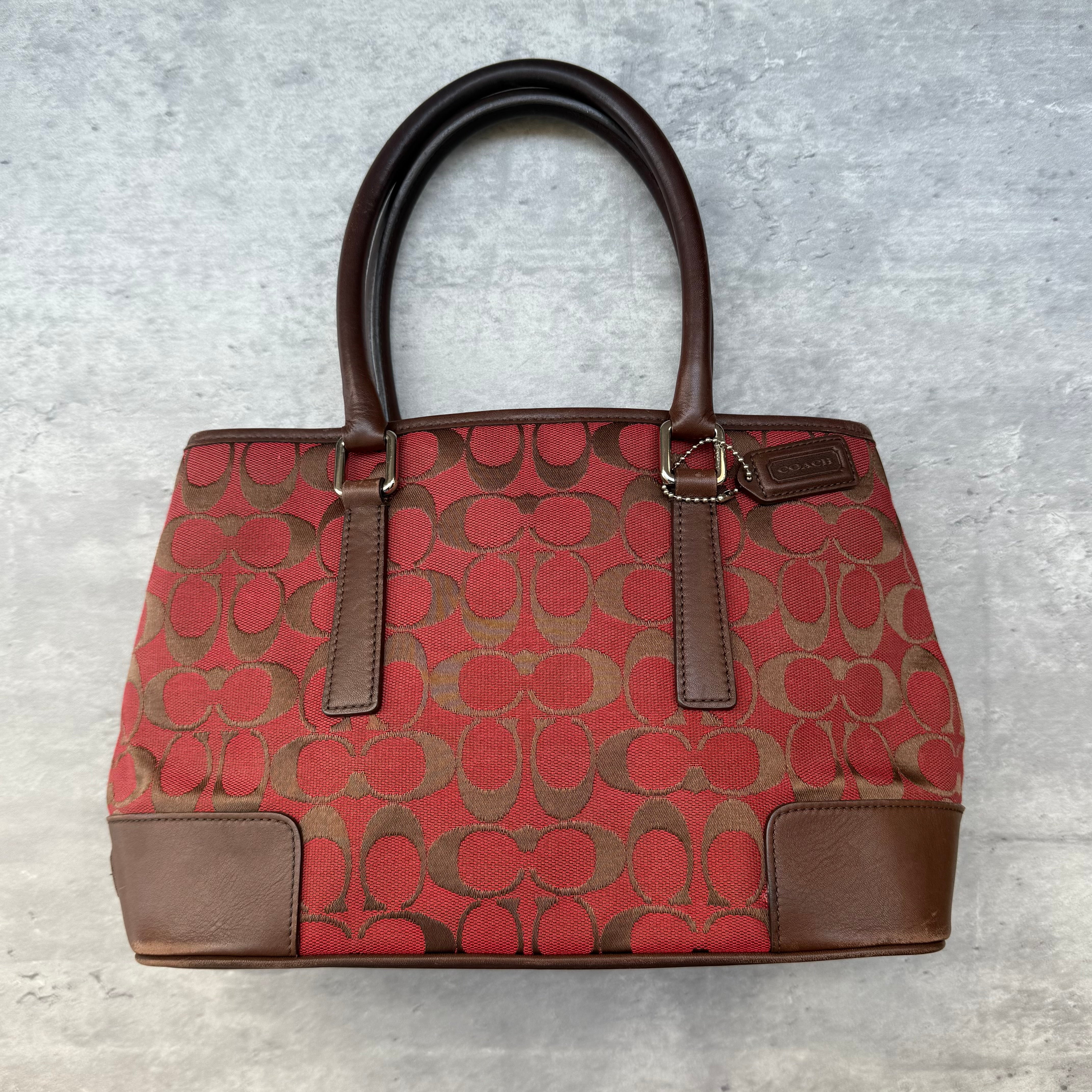 Coach Signature Canvas Handbag in red and brown with leather trim and dual handles, featuring spacious beige-lined interior.