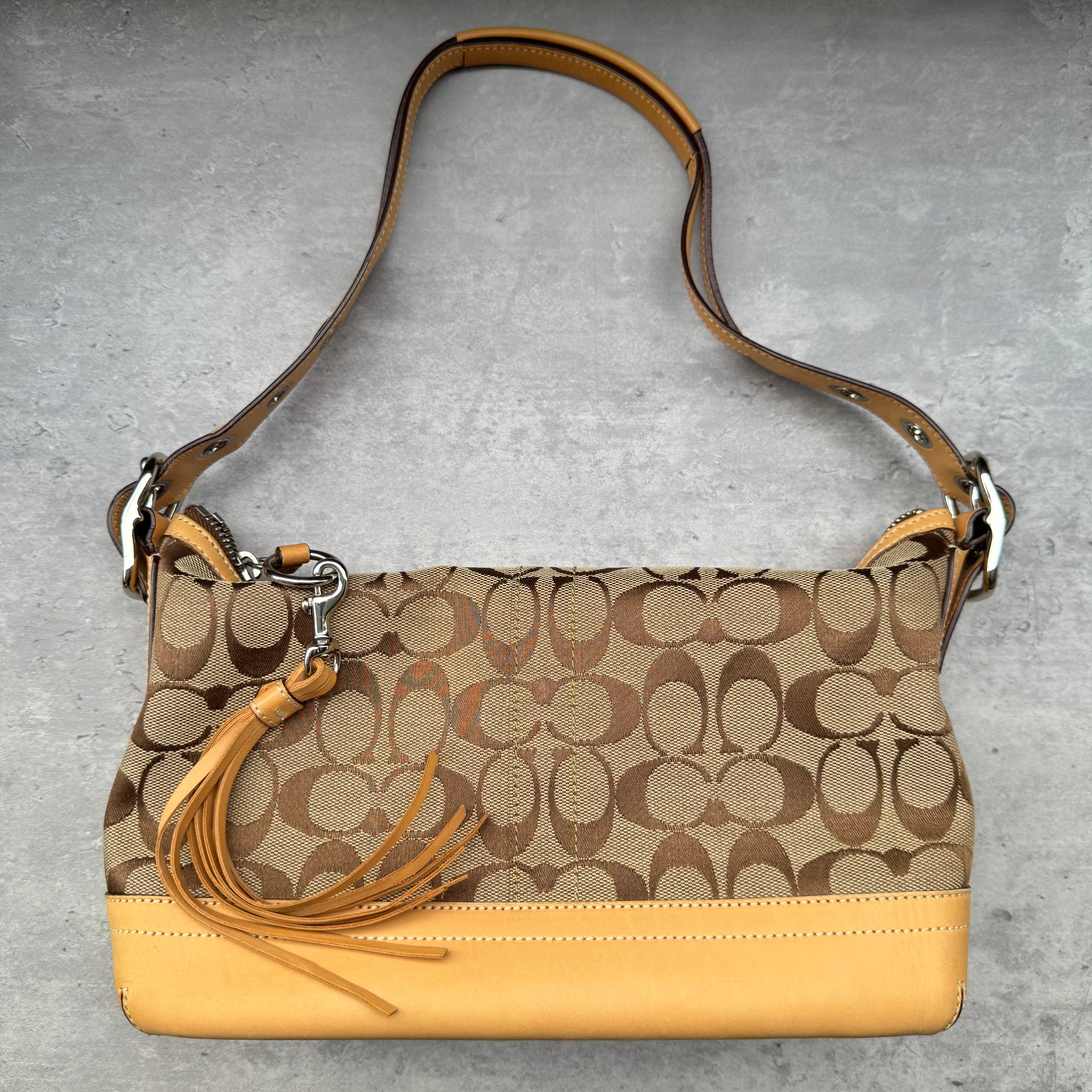 Coach Signature Coated Canvas Tassel Shoulder Bag in brown monogram print with tan leather trim and tassel detail.