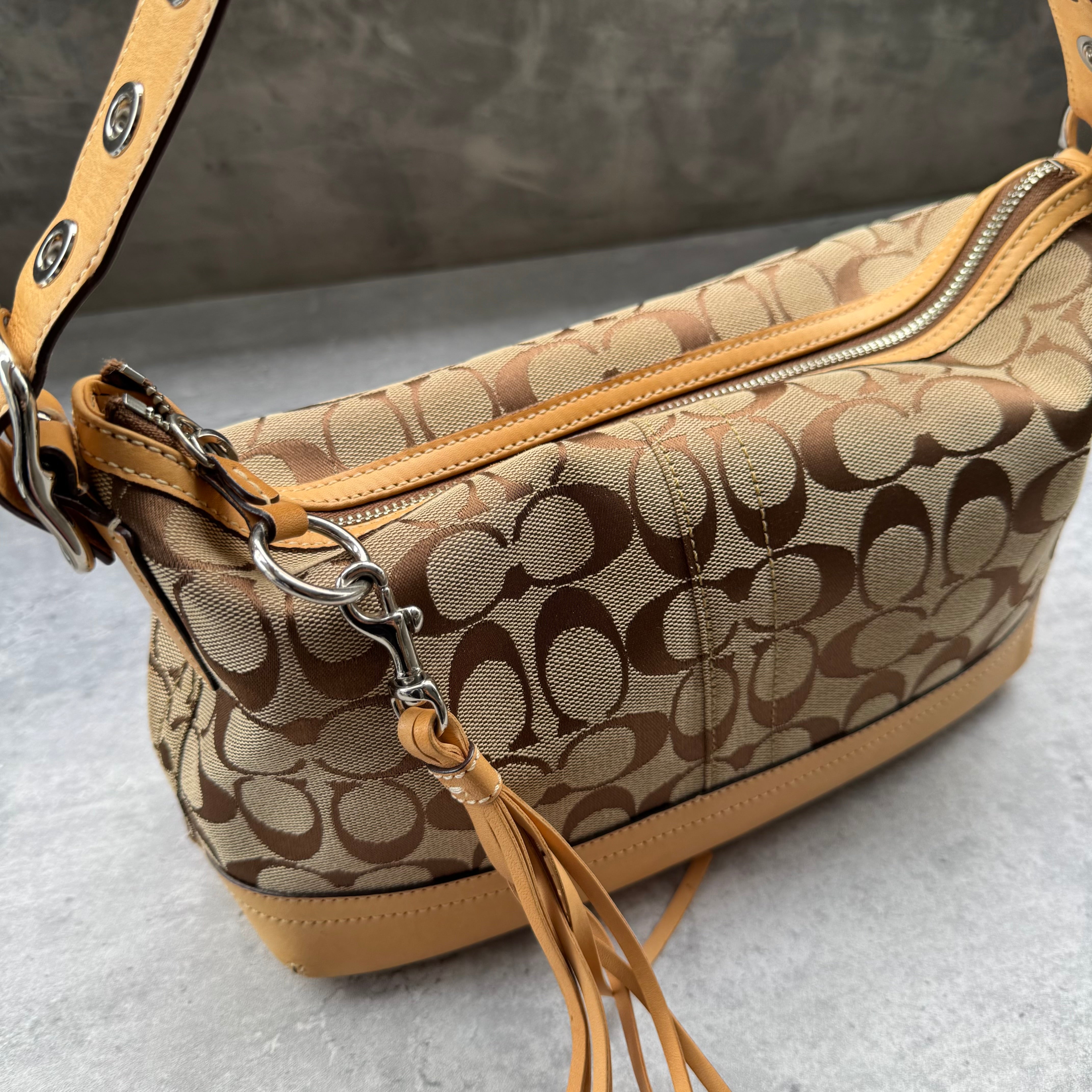 Coach Signature Coated Canvas Tassel Shoulder Bag in brown monogram print with tan leather trim and tassel detail.